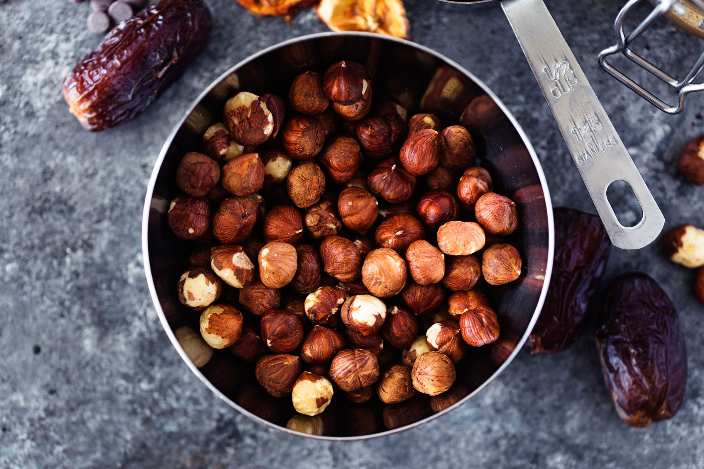 Whole hazelnuts in a metal bowl, surrounded by dates and other ingredients.