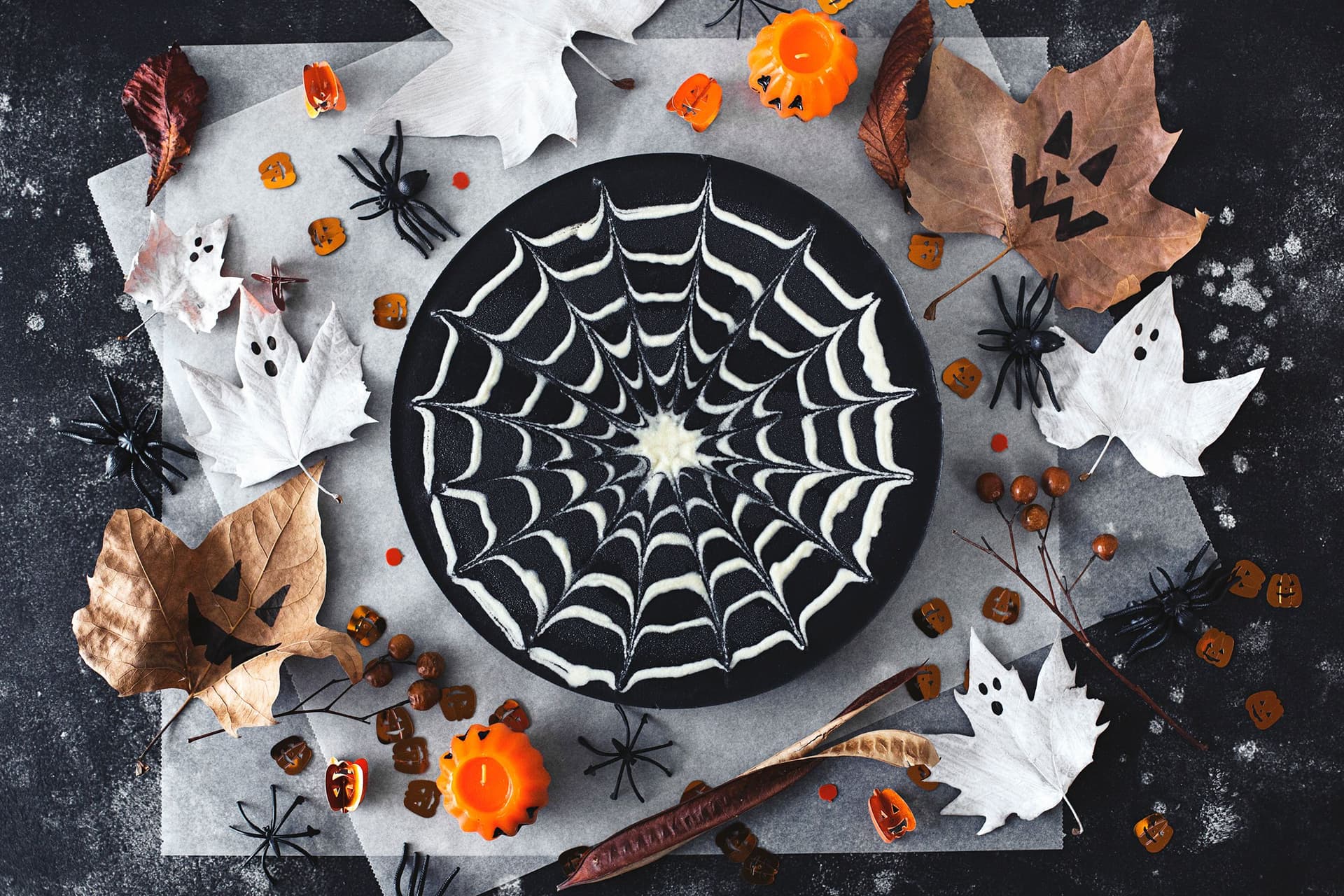 A double chocolate Halloween cheesecake with a spiderweb pattern surrounded by pumpkins, spiders and festive decorations.