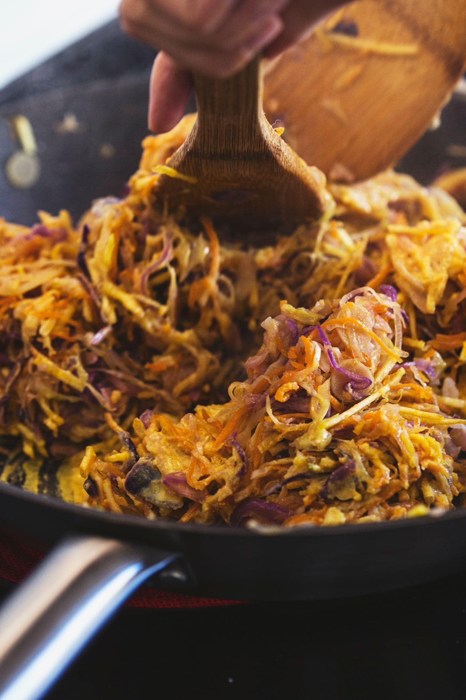 Wooden spoon stirring golden sautéed vegetables in a pan.