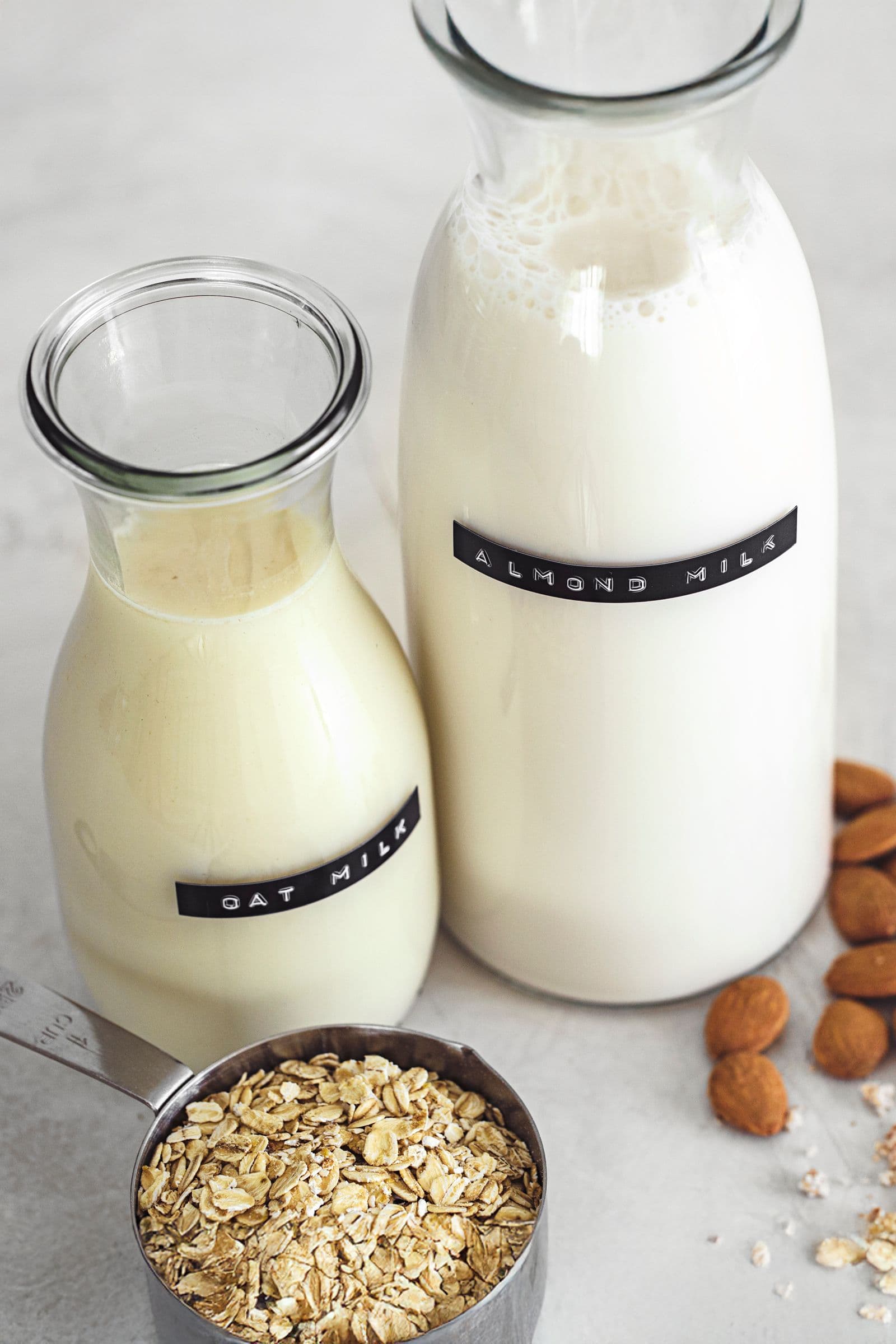 Ingredientes básicos para fazer leite vegetal, com frascos de leite de aveia e de amêndoa, aveia em flocos e amêndoas inteiras.