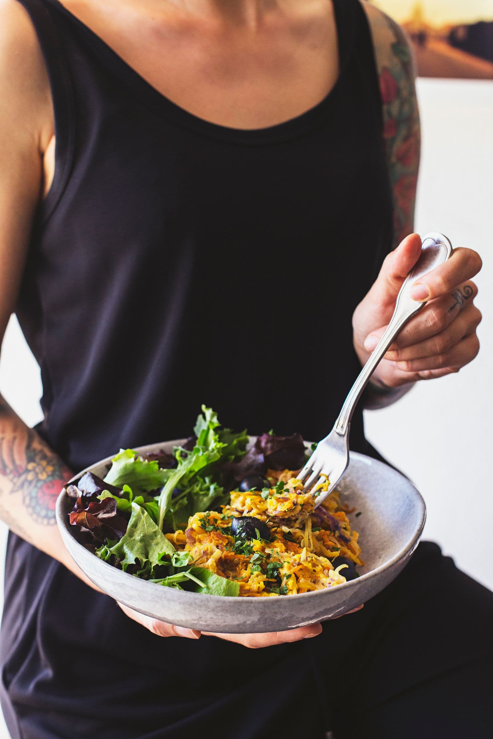 Pessoa a segurar uma tigela de vegetais à Brás com salada verde, pronta a comer.