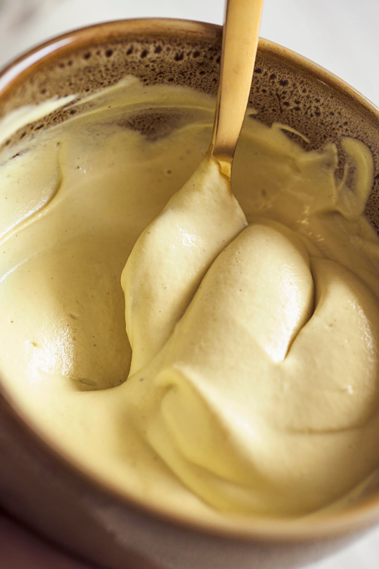 Mistura cremosa de iogurte vegan de manga a ser mexida com colher dourada.