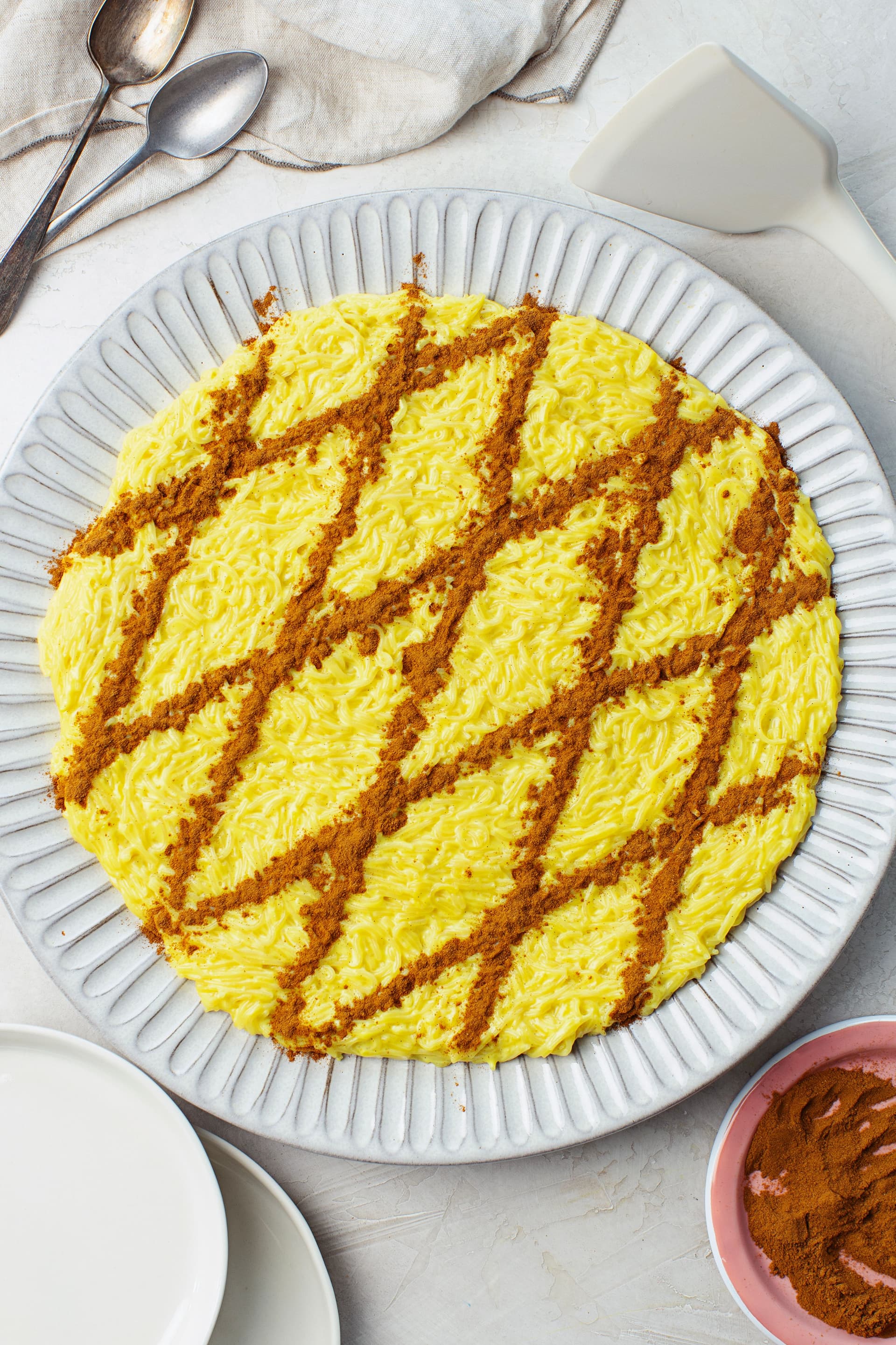 Aletria vegan pronta a servir, decorada com linhas diagonais de canela, com colheres e guardanapo ao lado.