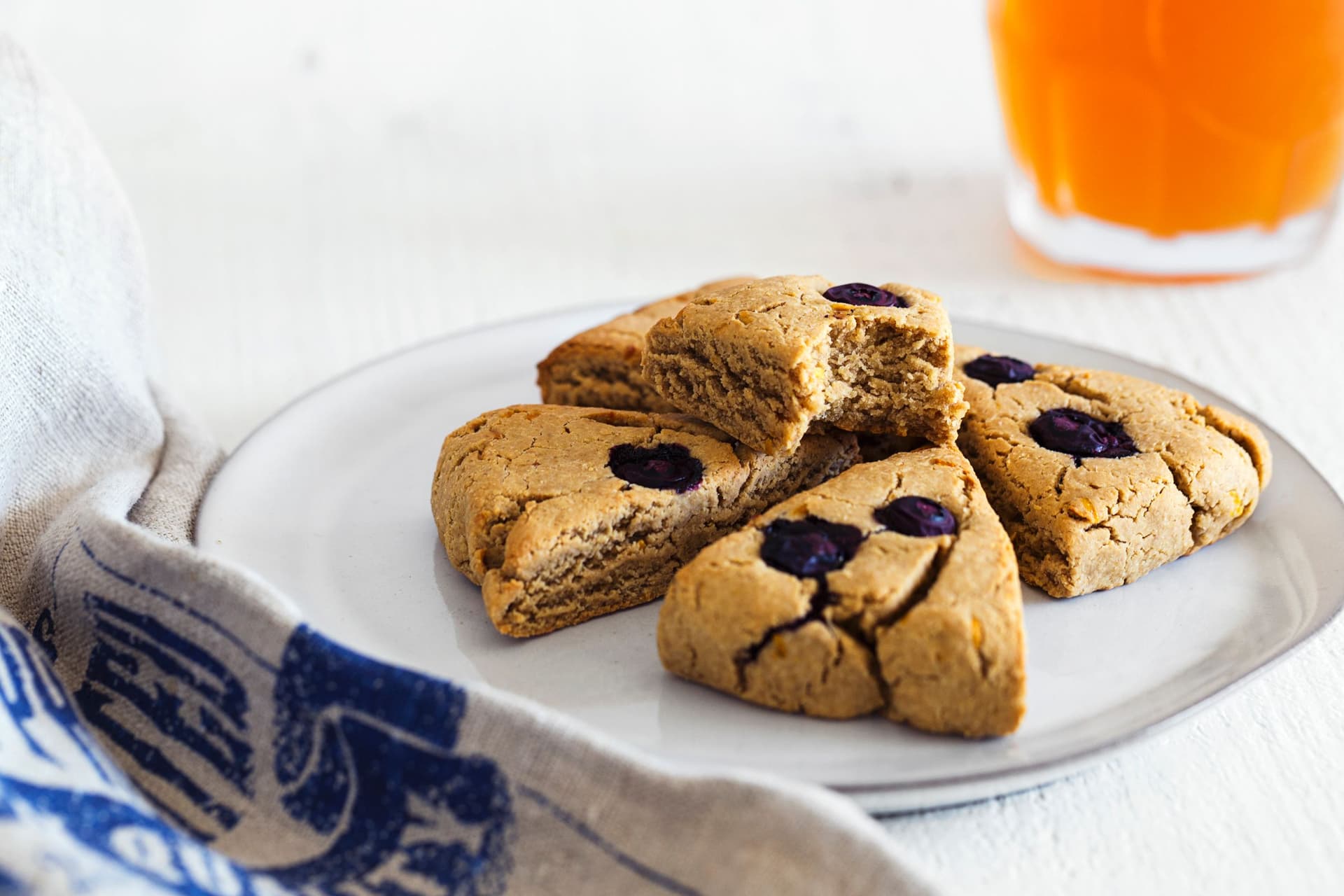 Scones veganos de limão e mirtilos servido com creme num prato, copo de chá gelado caseiro ao fundo.