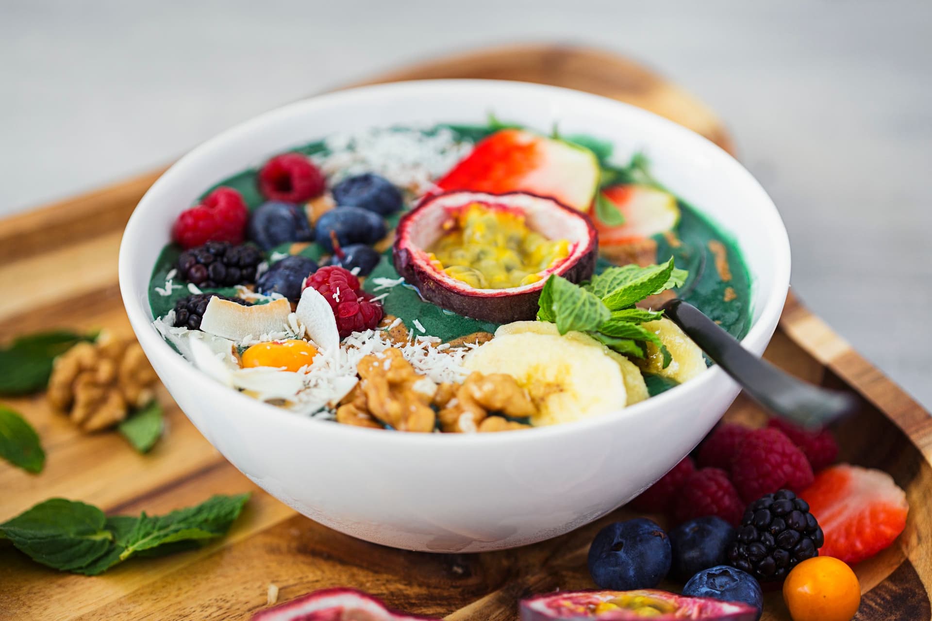 Spirulina banana nicecream in a bowl on a wooden tray with fruit and walnut toppings.