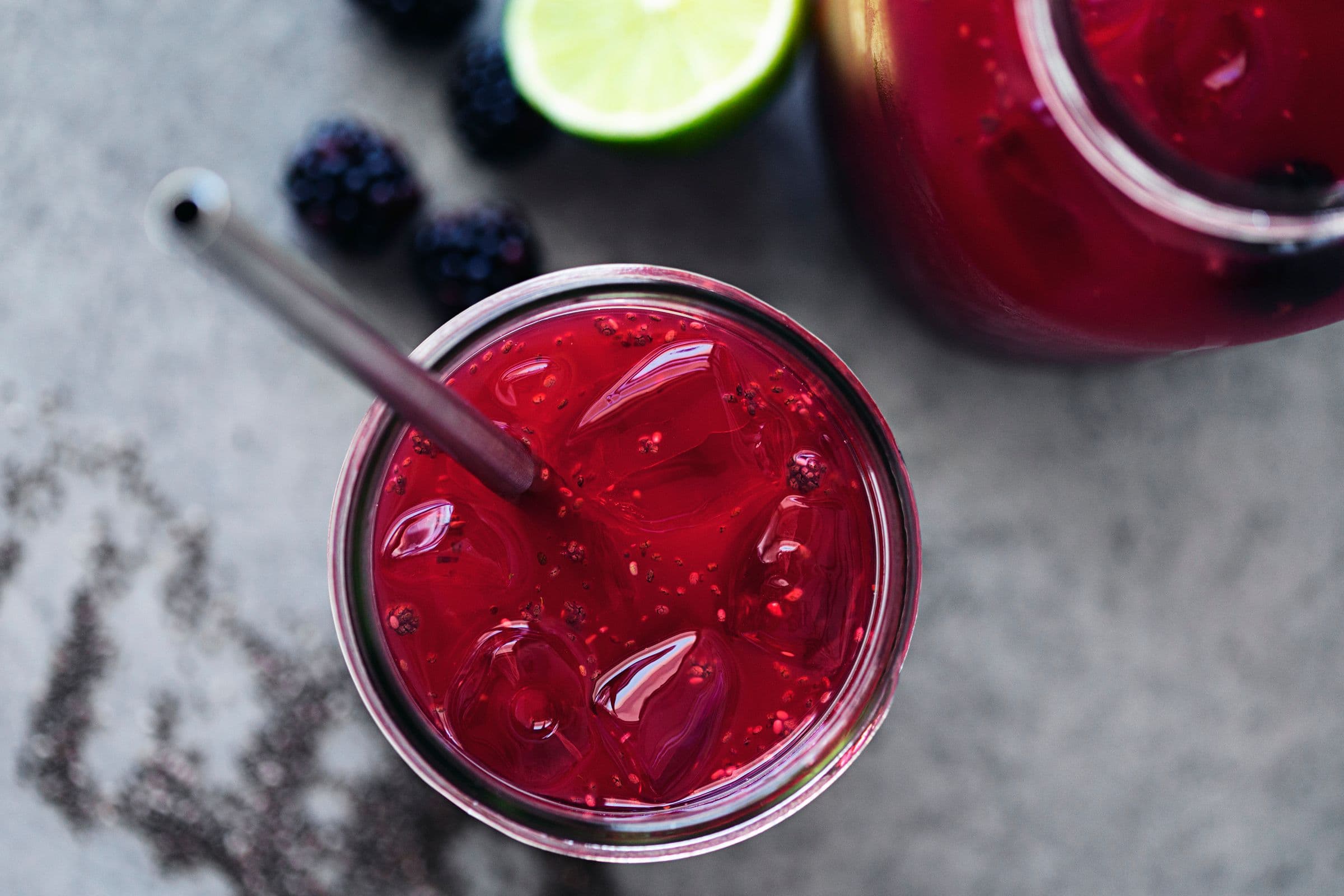 Overhead of a glass filled with vibrant blackberry chia fresca, ice cubes, and a metal straw.