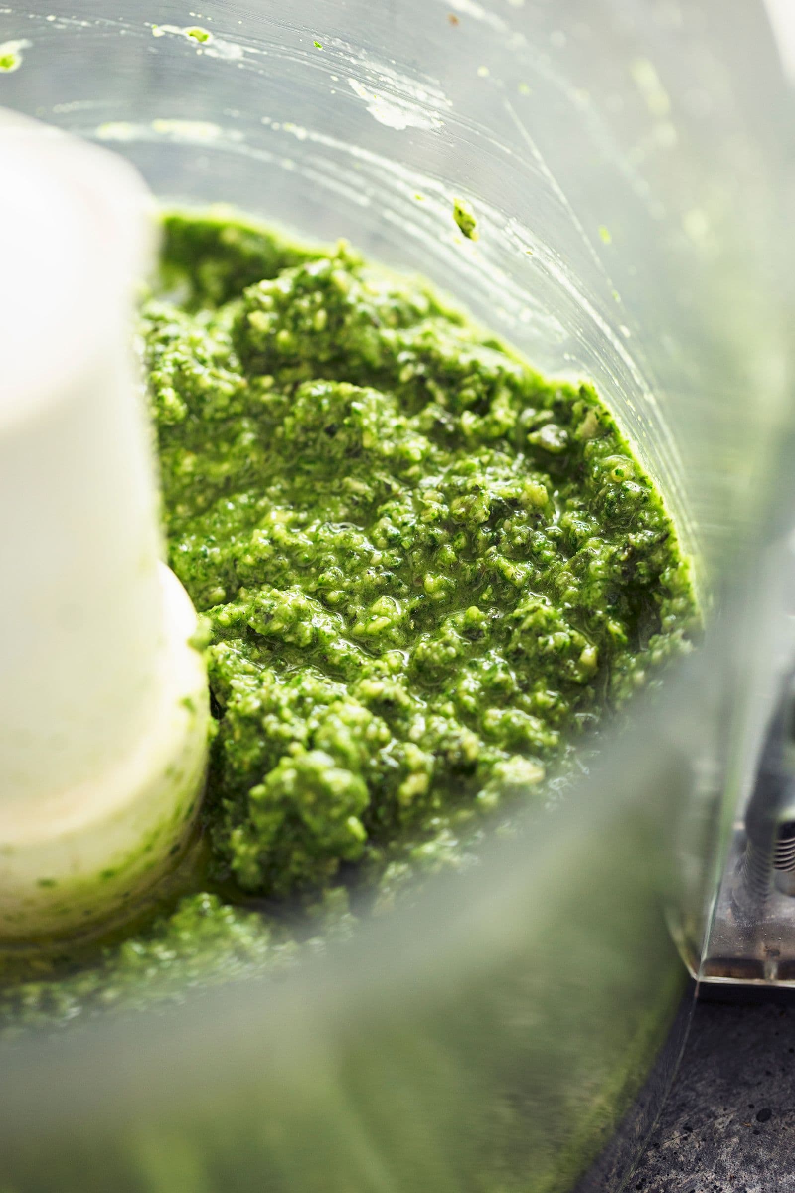 Smooth, vibrant green vegan pesto mixture freshly blended in a food processor.