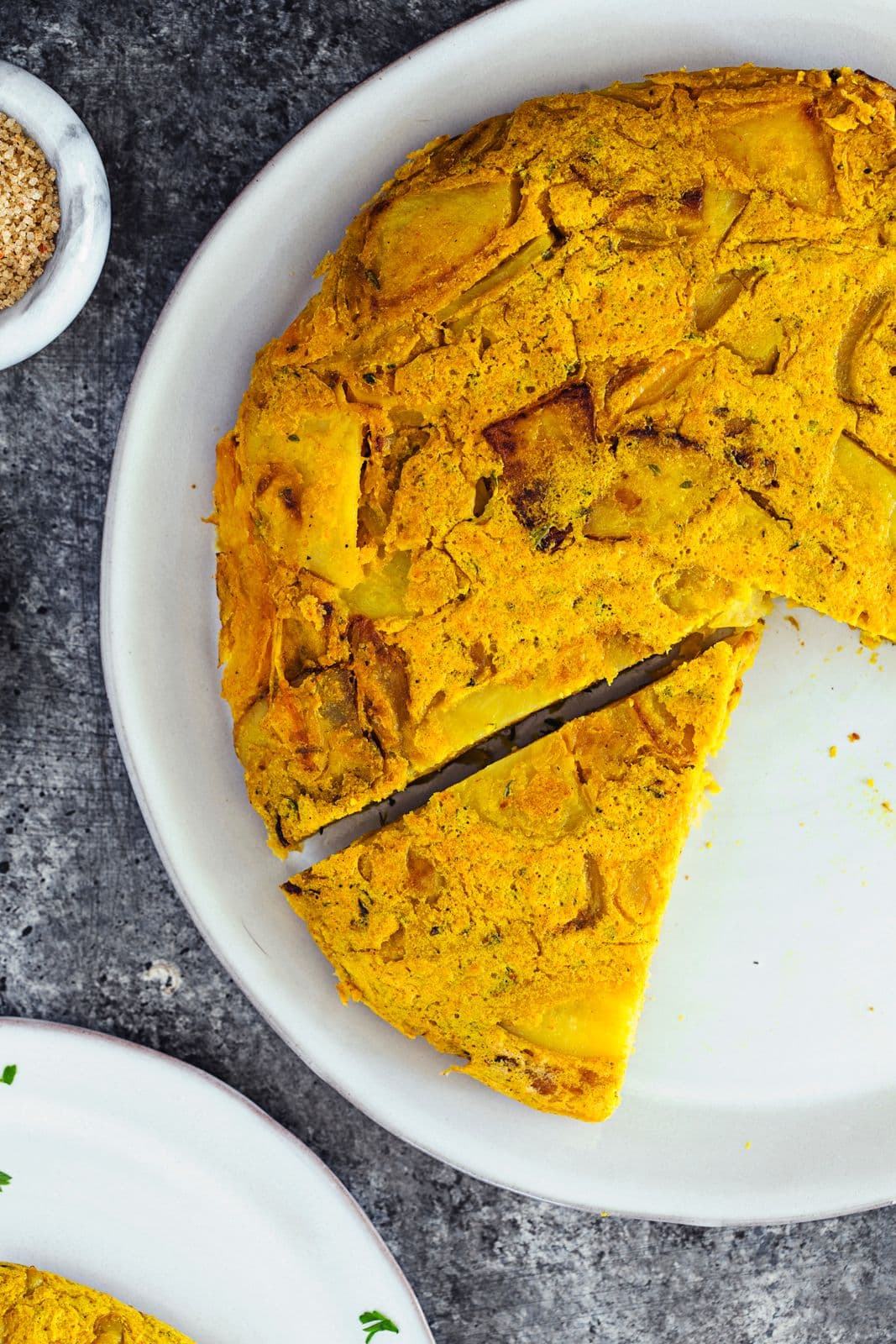 Tortilha vegan servida inteira com uma fatia retirada, num prato branco com salsa.