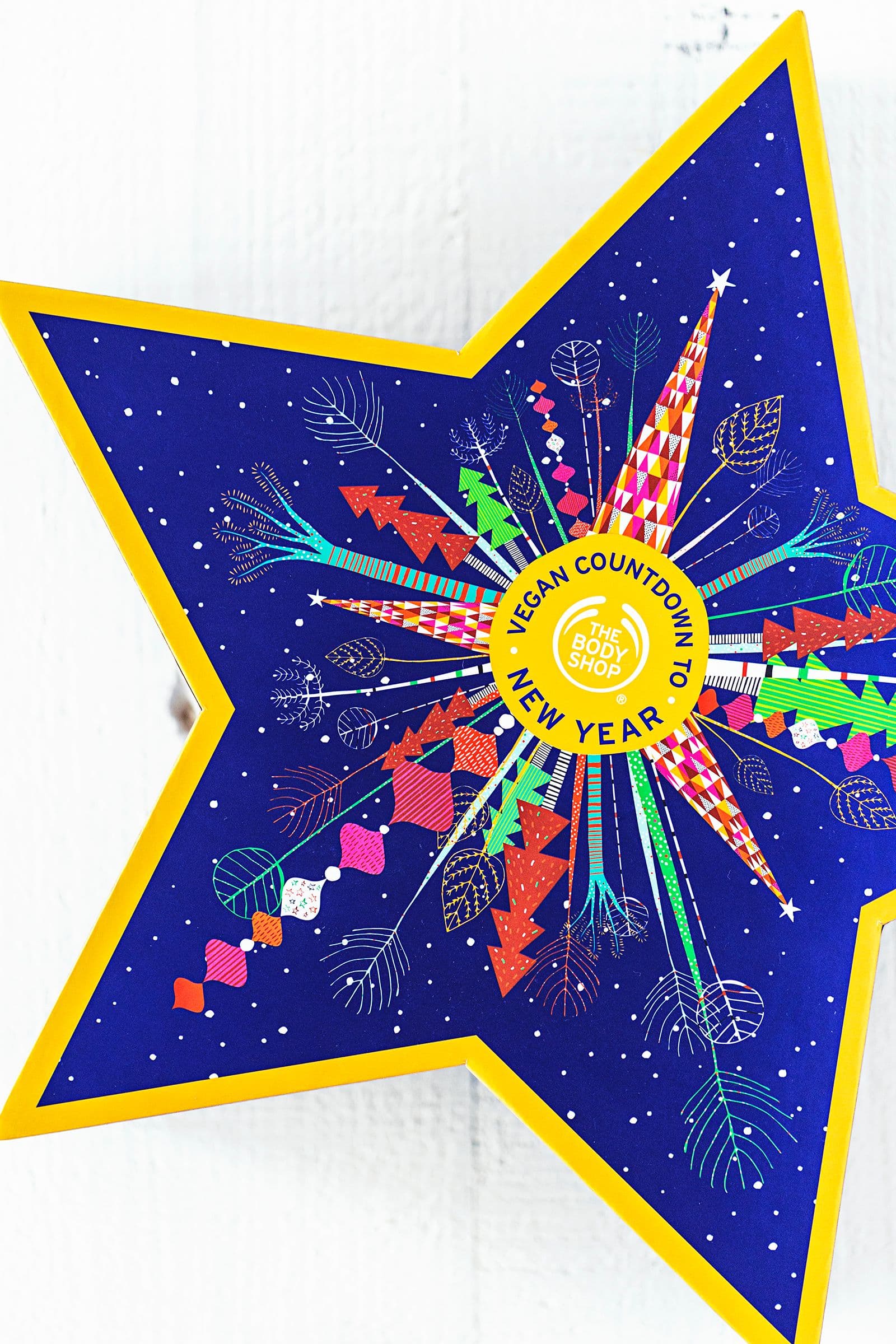 Caixa de presente em forma de estrela azul com detalhes coloridos e texto “Vegan Countdown to New Year” da The Body Shop.