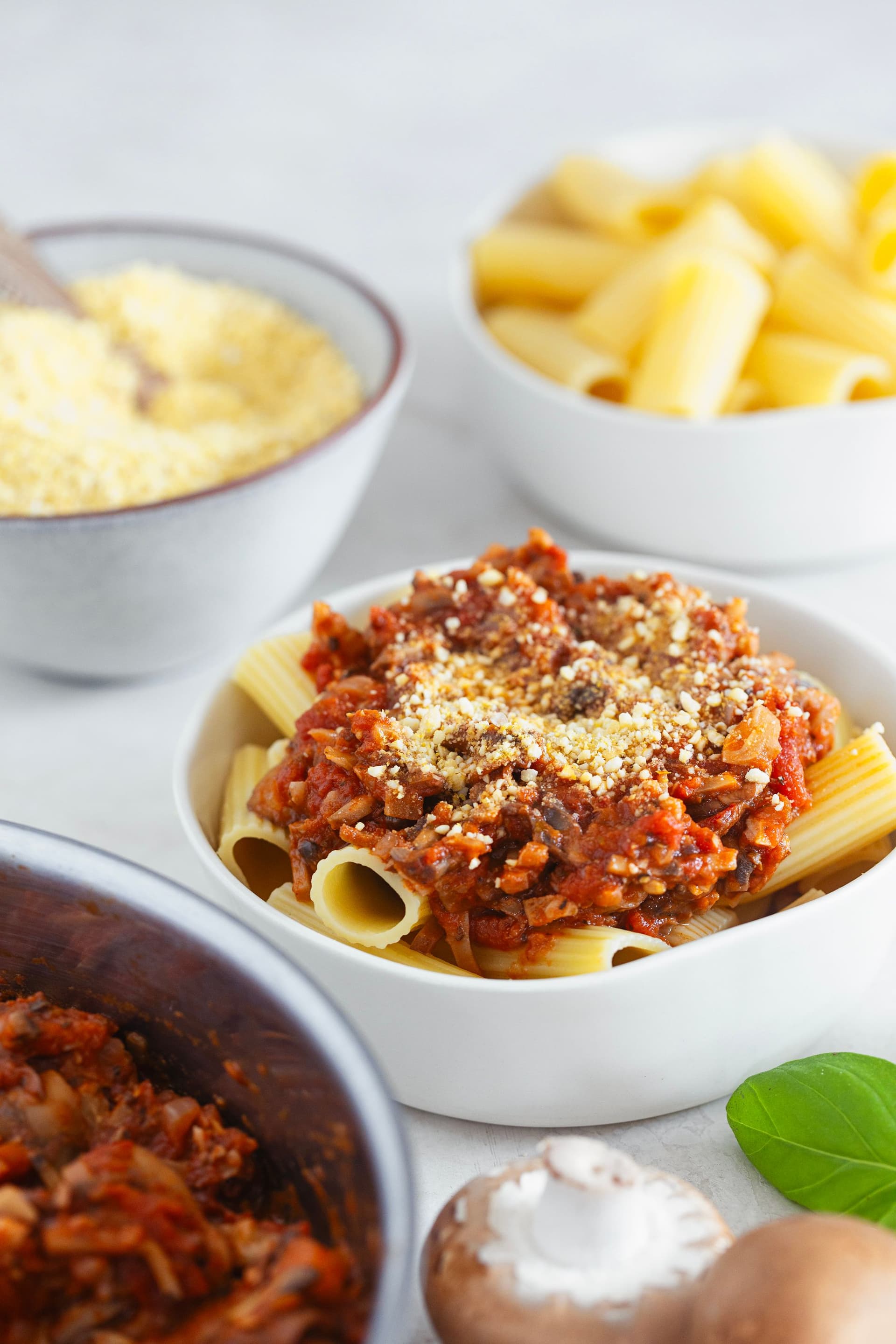 Bowl of pasta topped with spicy bolognese and garnished with vegan cashew parmesan.