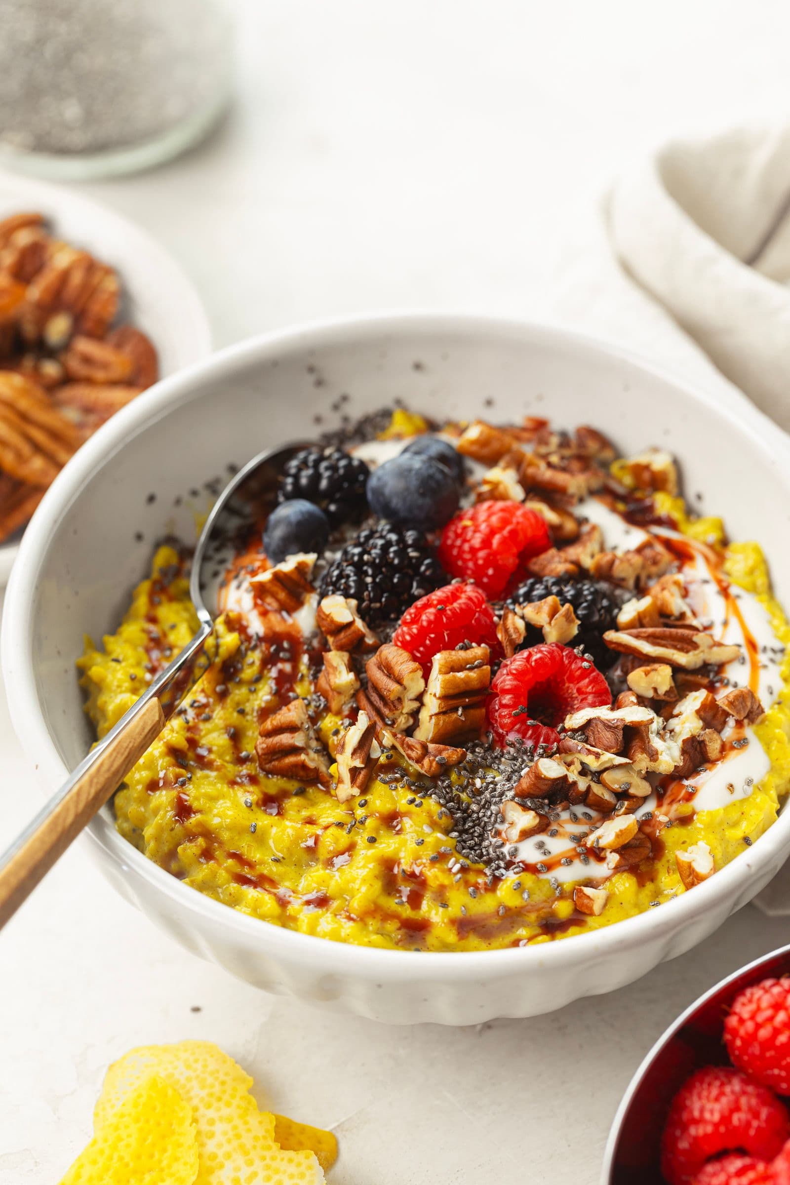 Golden oatmeal with chia, pecans, berries, plant yogurt and date syrup, served in a white bowl with a spoon