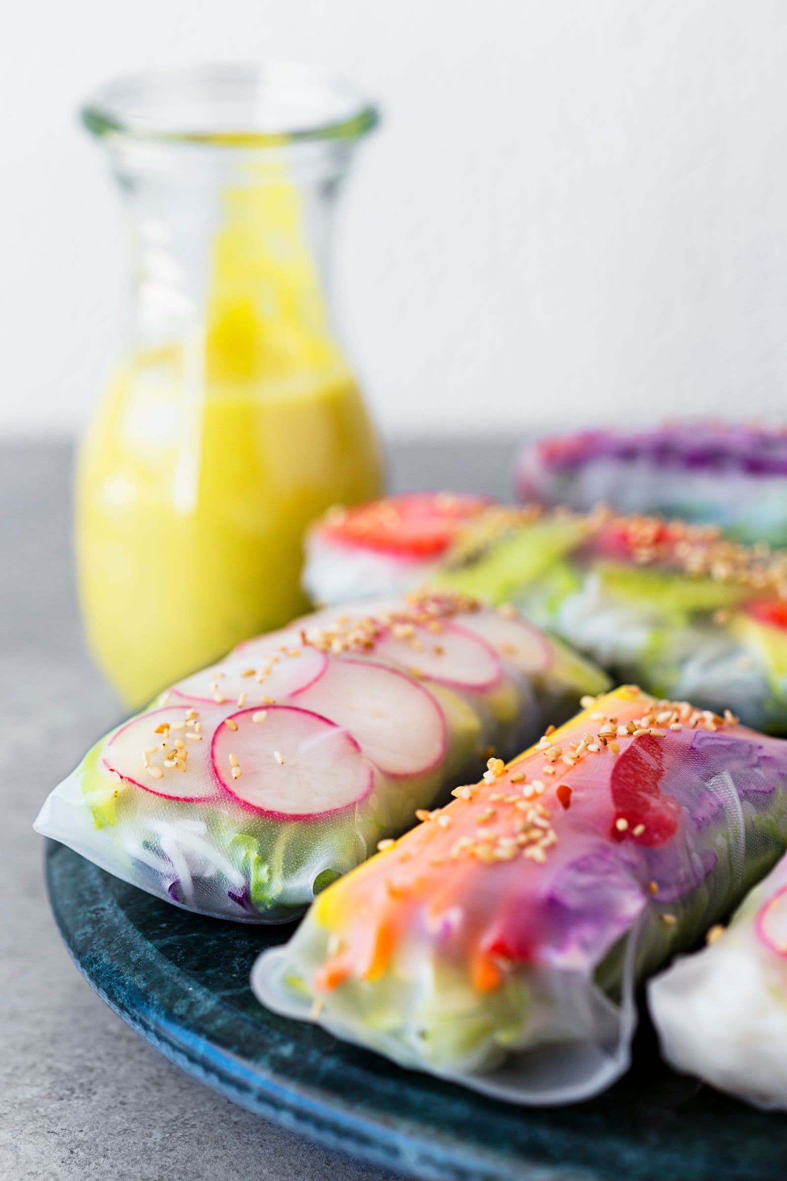 Finished rainbow spring rolls served with a jar of mango tahini sauce in the background.