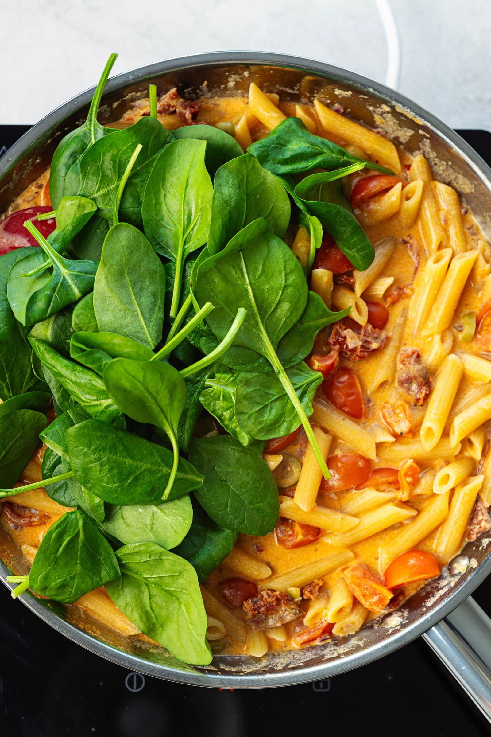 Fresh spinach leaves added to the almost-cooked creamy tomato penne in a large pan