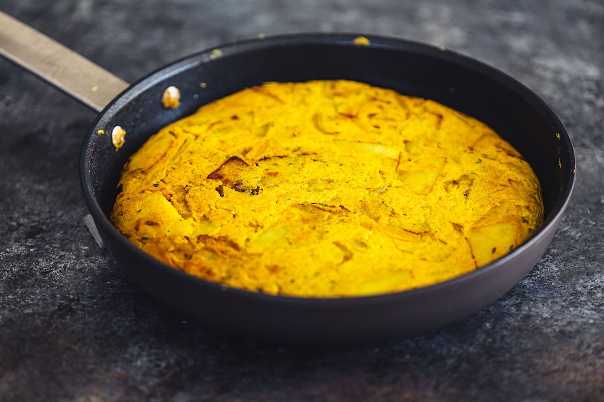 Tortilha espanhola vegan cozinhada numa frigideira preta.