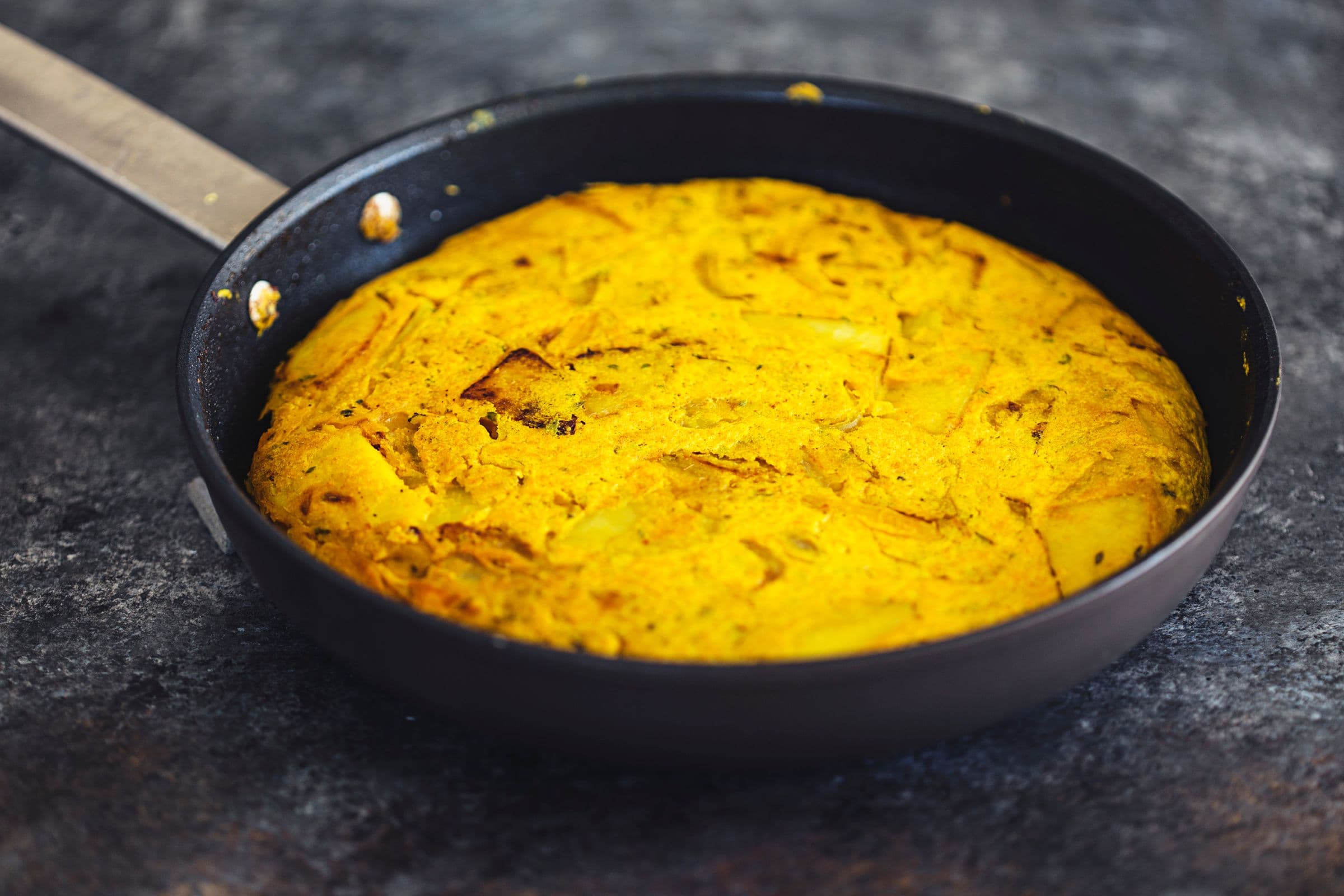 Tortilha espanhola vegan cozinhada numa frigideira preta.