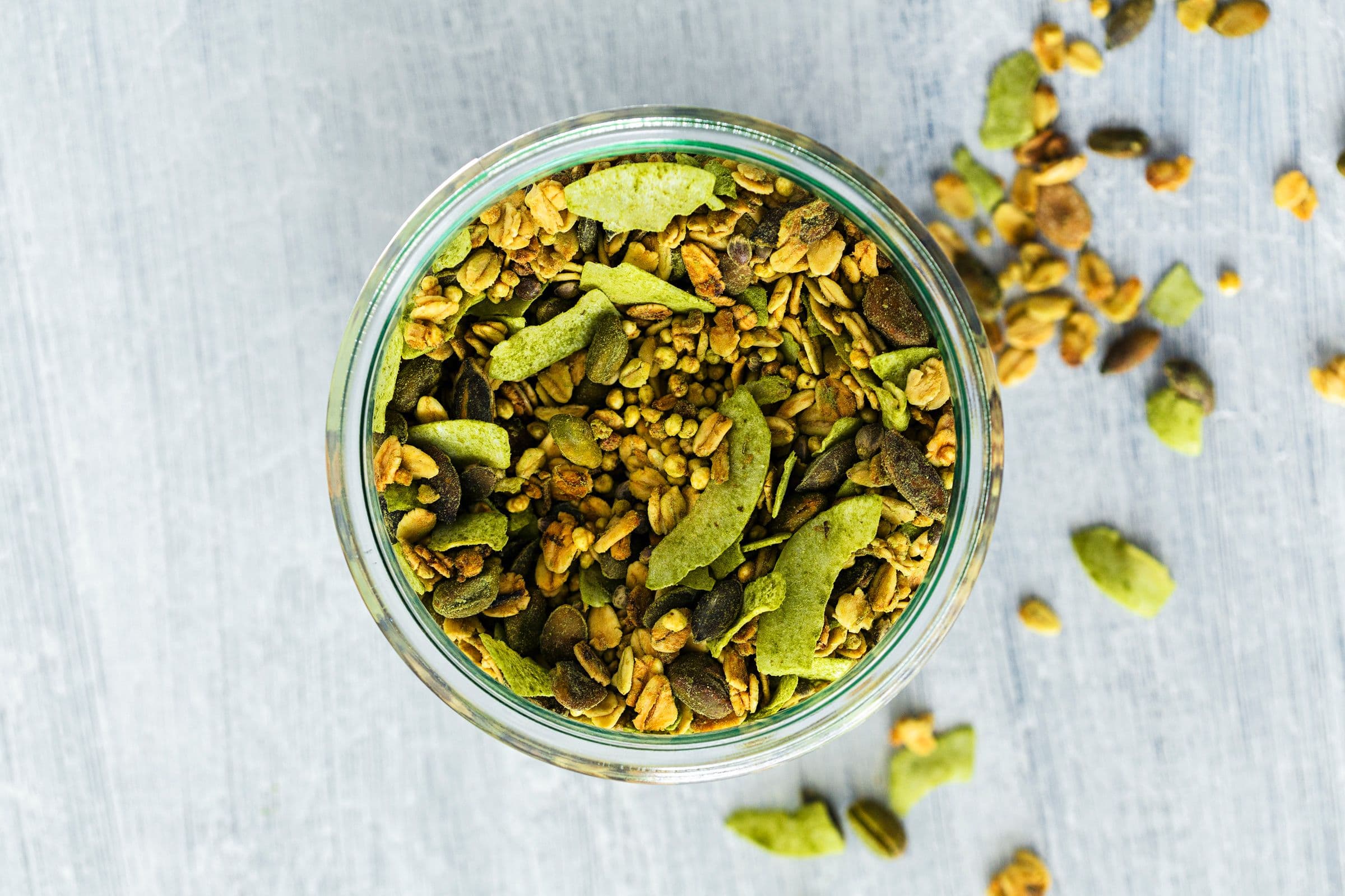 Overhead view of a jar filled with green coconut and lime granola with wheatgrass and seeds.