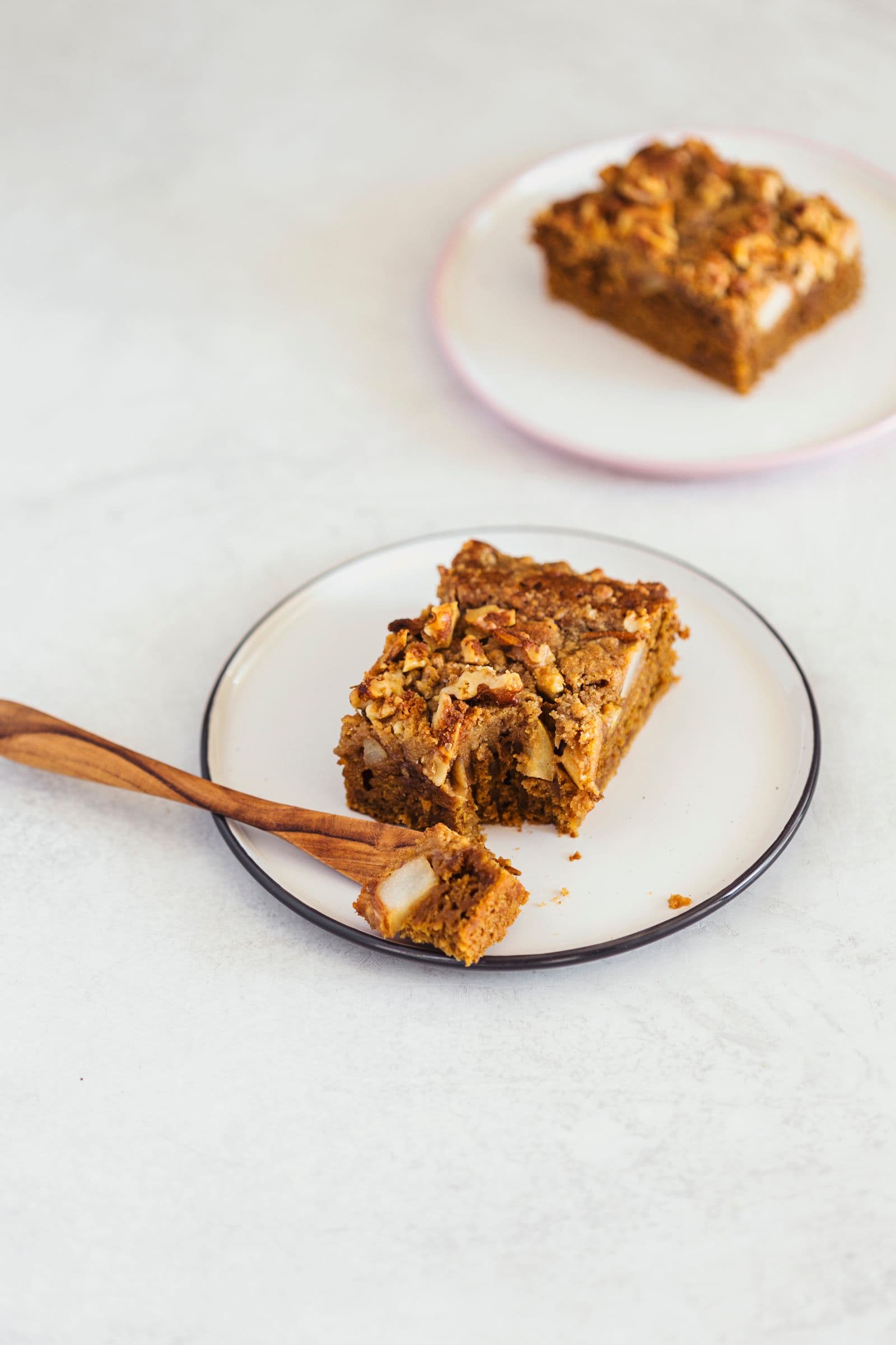 Uma fatia de bolo de café com uma dentada, servida num prato com garfo de madeira.