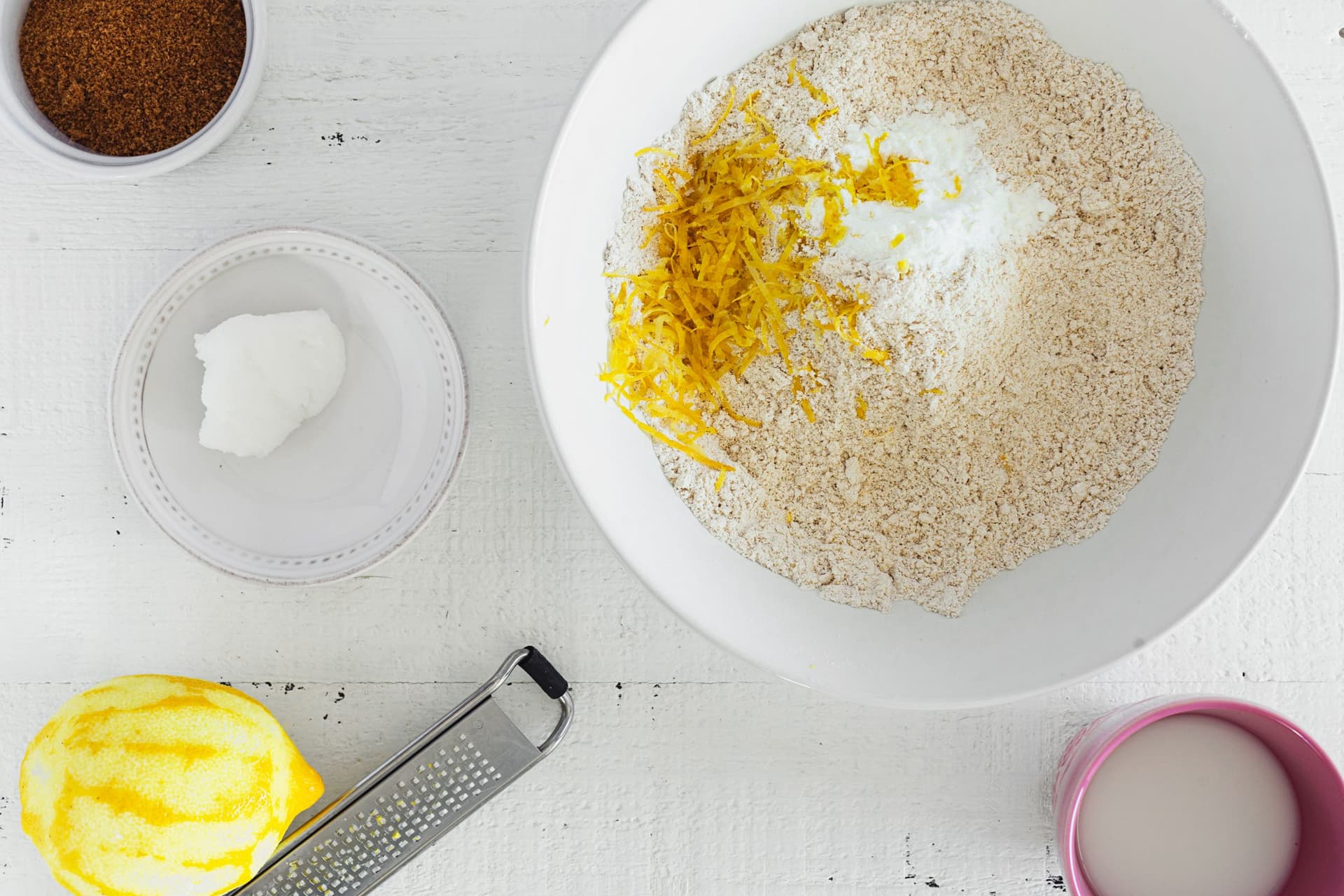 Taça com raspa limão e farinha de aveia a serem misturados para preparar a massa dos scones veganos.