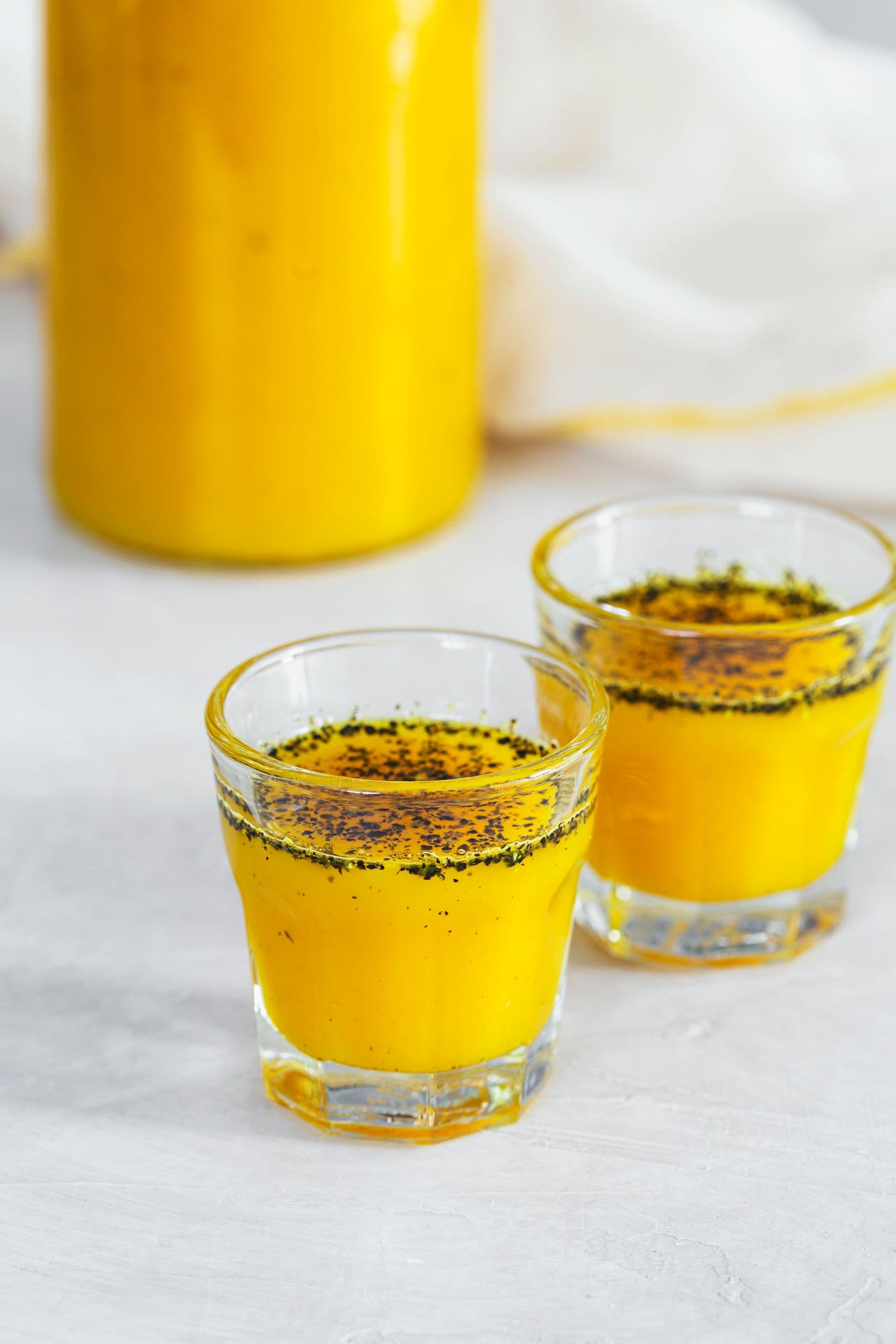 Garrafa e dois copinhos cheios de xarope de gengibre e curcuma.