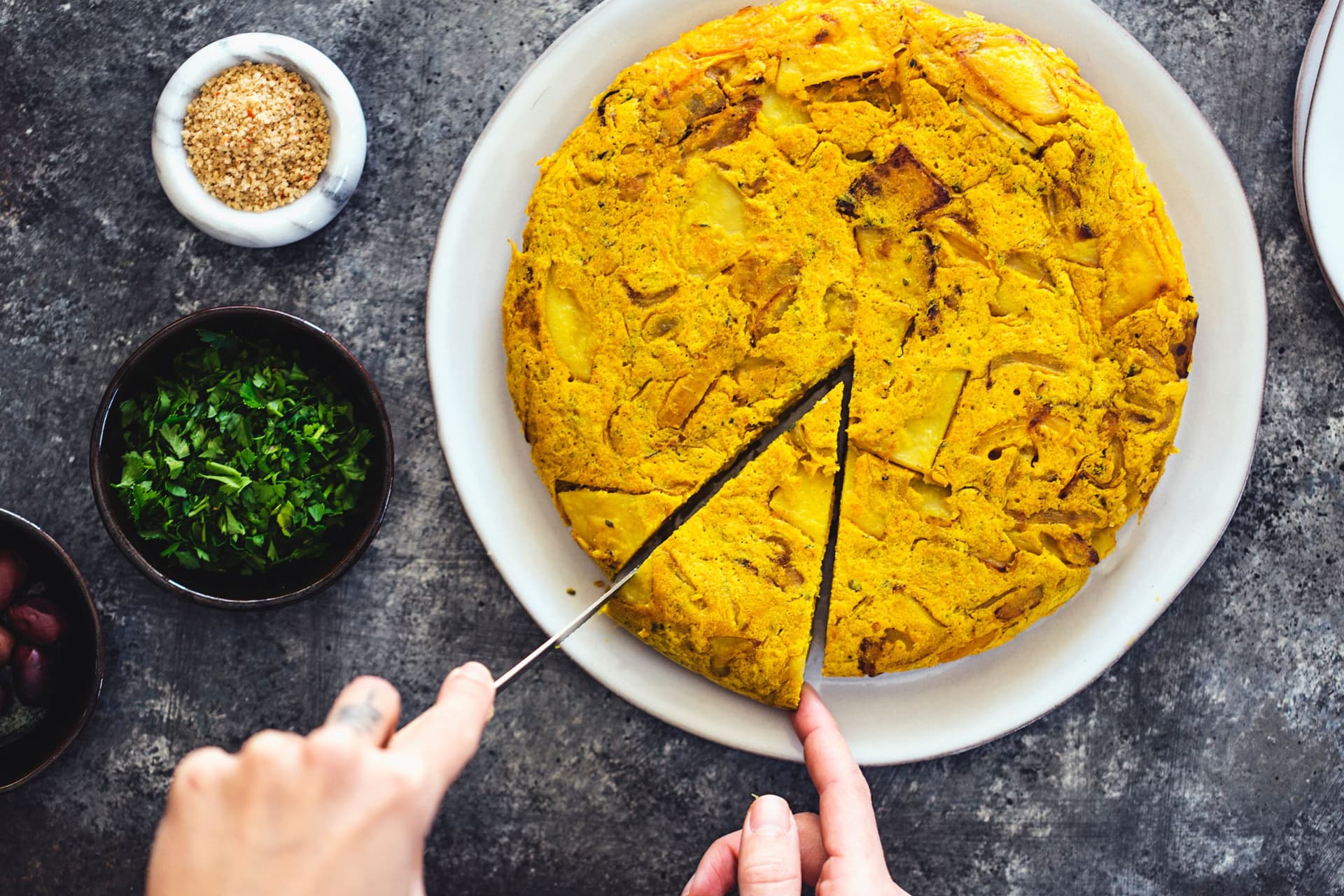 Tortilha inteira num prato branco com taças de salsa e sal marinho com piri piri ao lado.
