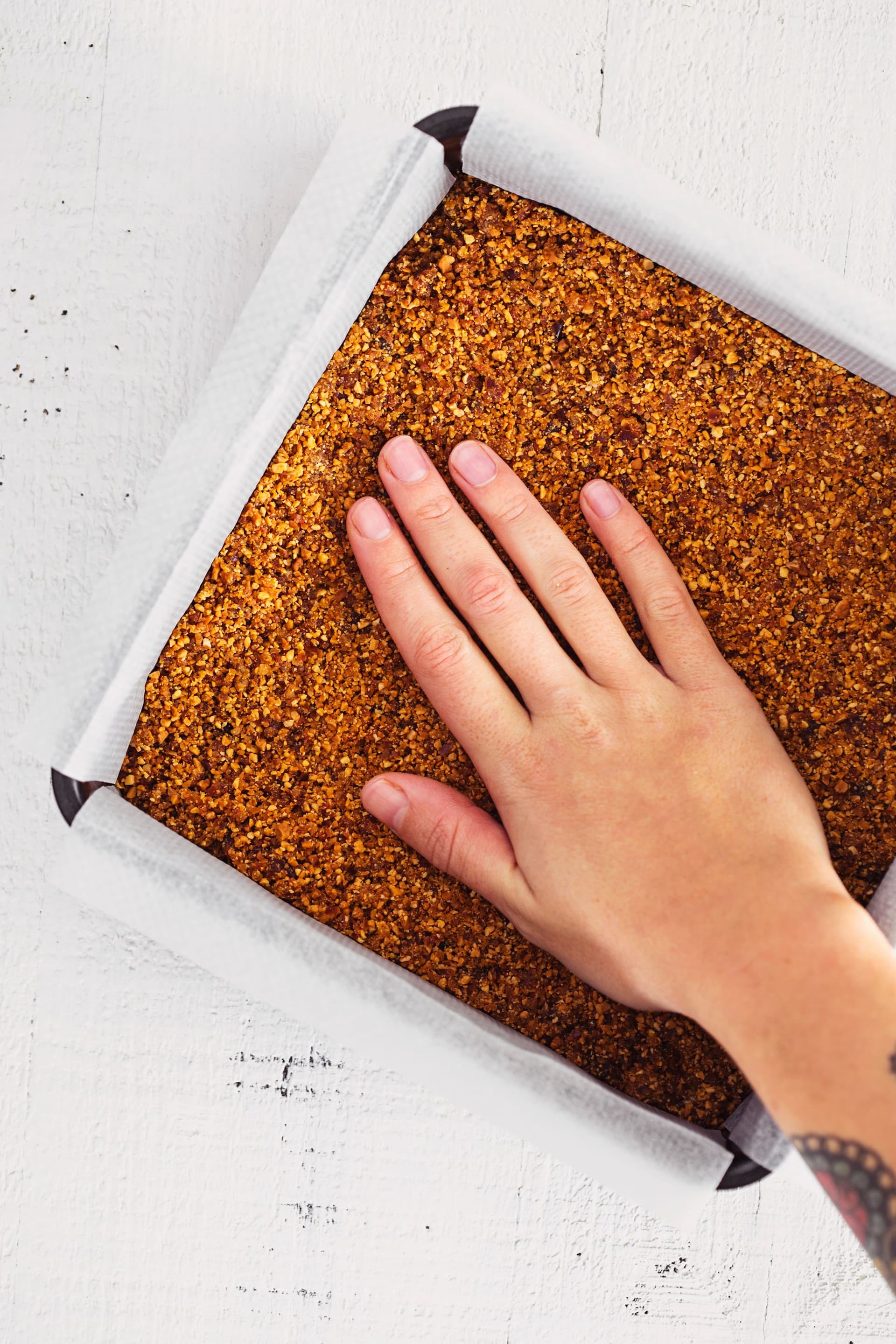 Hand pressing the crust mixture into a square baking tin.