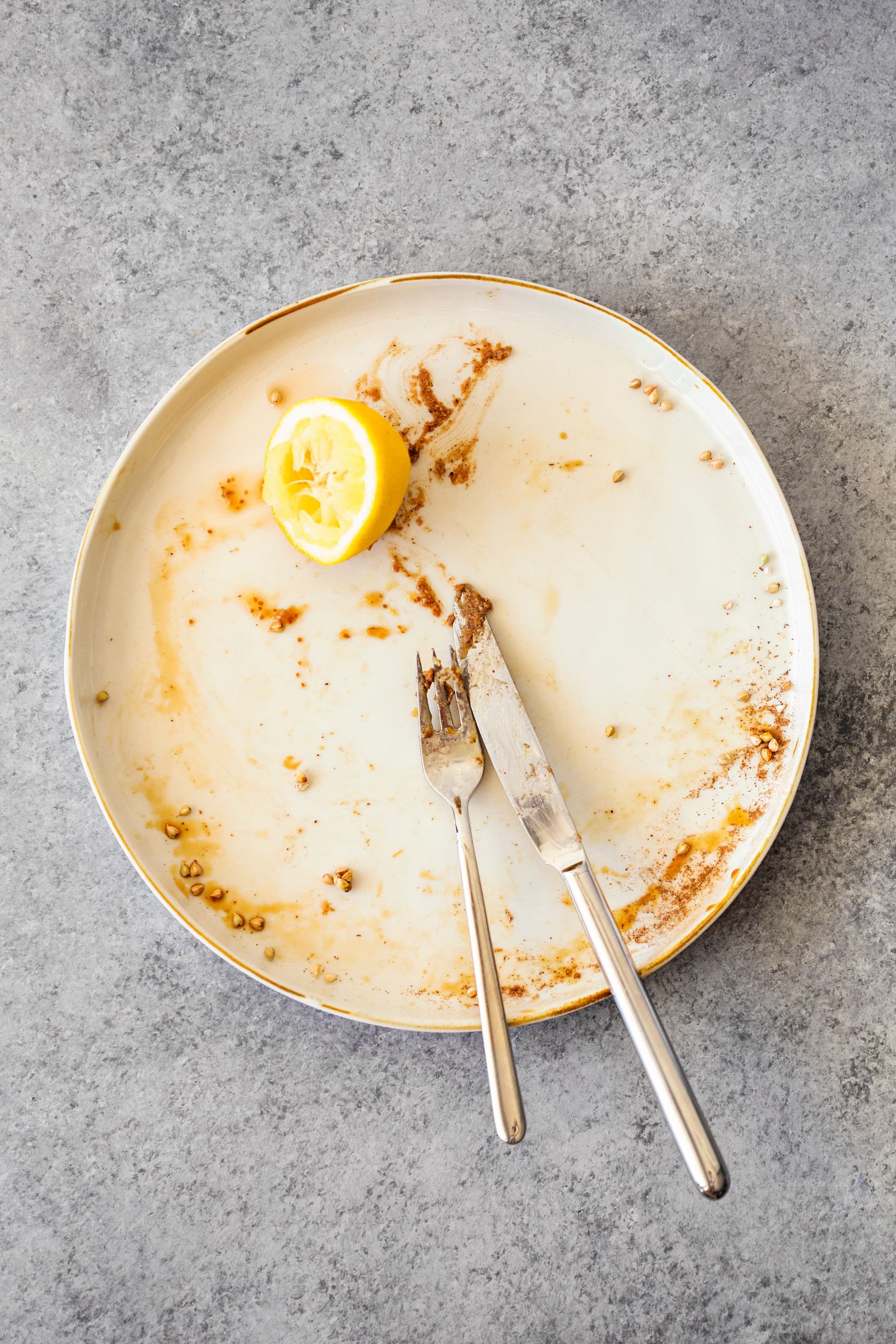 Empty plate with pancake crumbs, lemon slice and used cutlery.