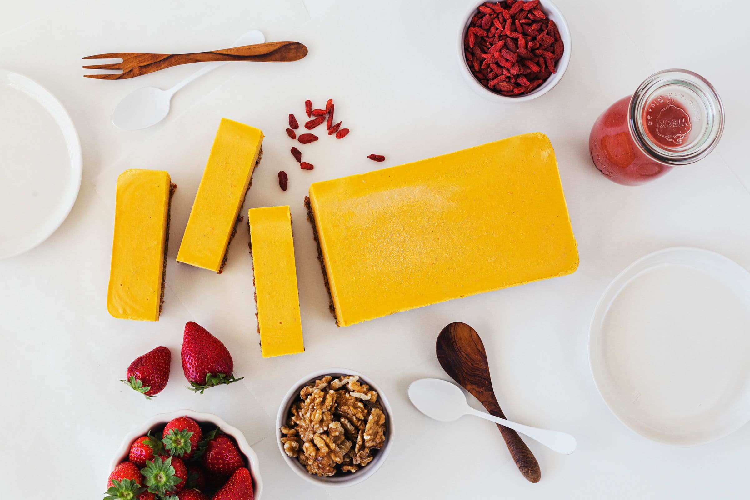 Rectangular orange cheesecake bar on a white table with goji berries and strawberries around it.