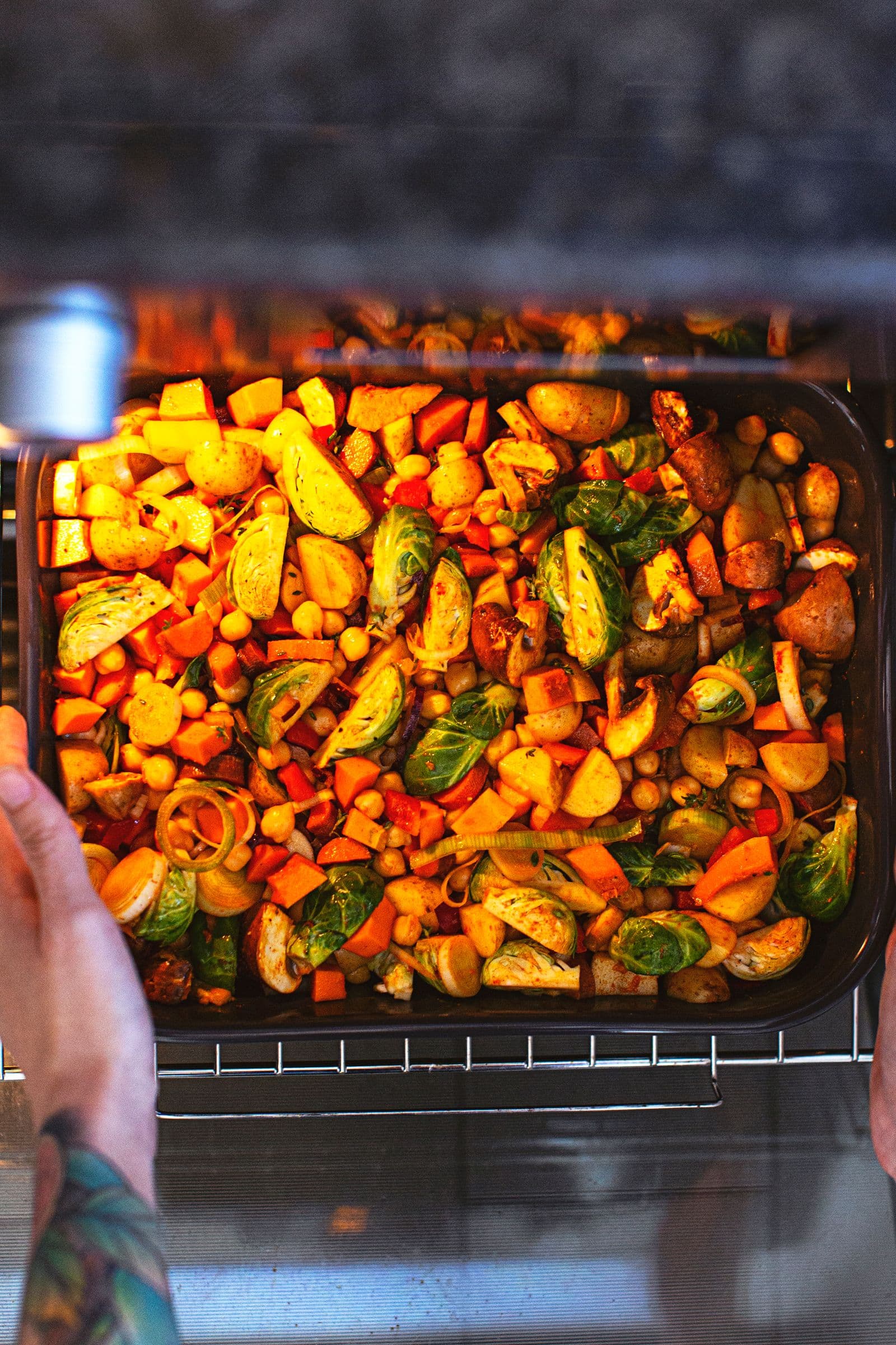 Hands sliding a baking dish of vegetables into the oven for a vegan savoury crumble.