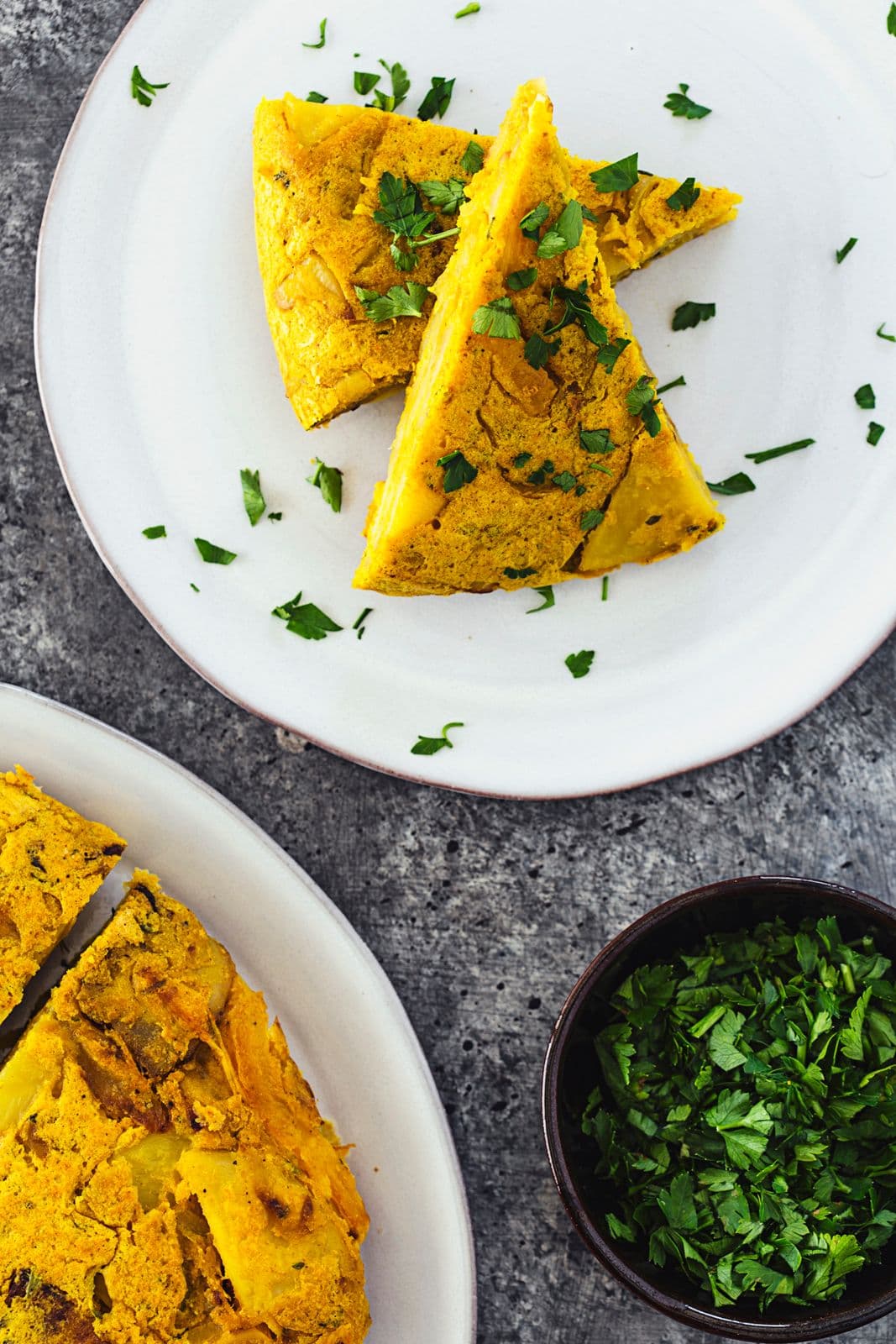 Duas fatias de tortilha espanhola vegan dispostas num prato branco, com salsa por cima.