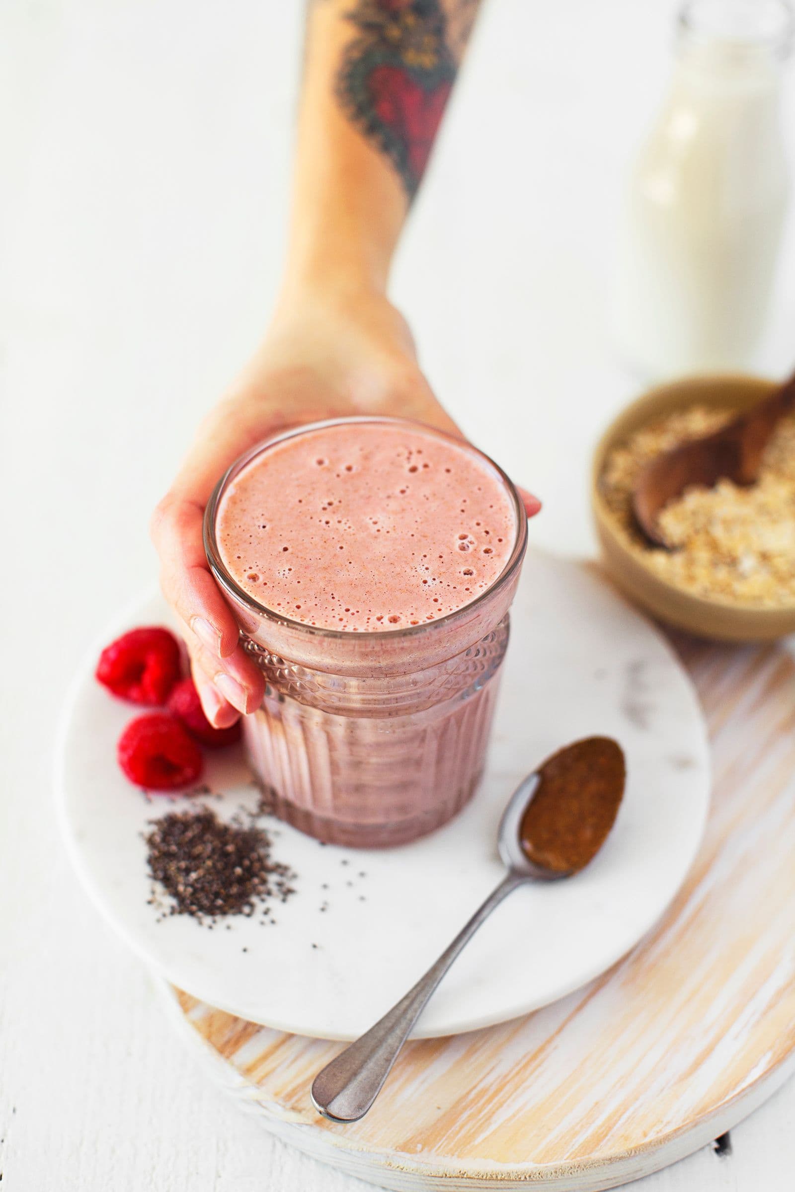 Mão a segurar um copo de batido rosa equilibrador hormonal ao lado dos ingredientes usados.