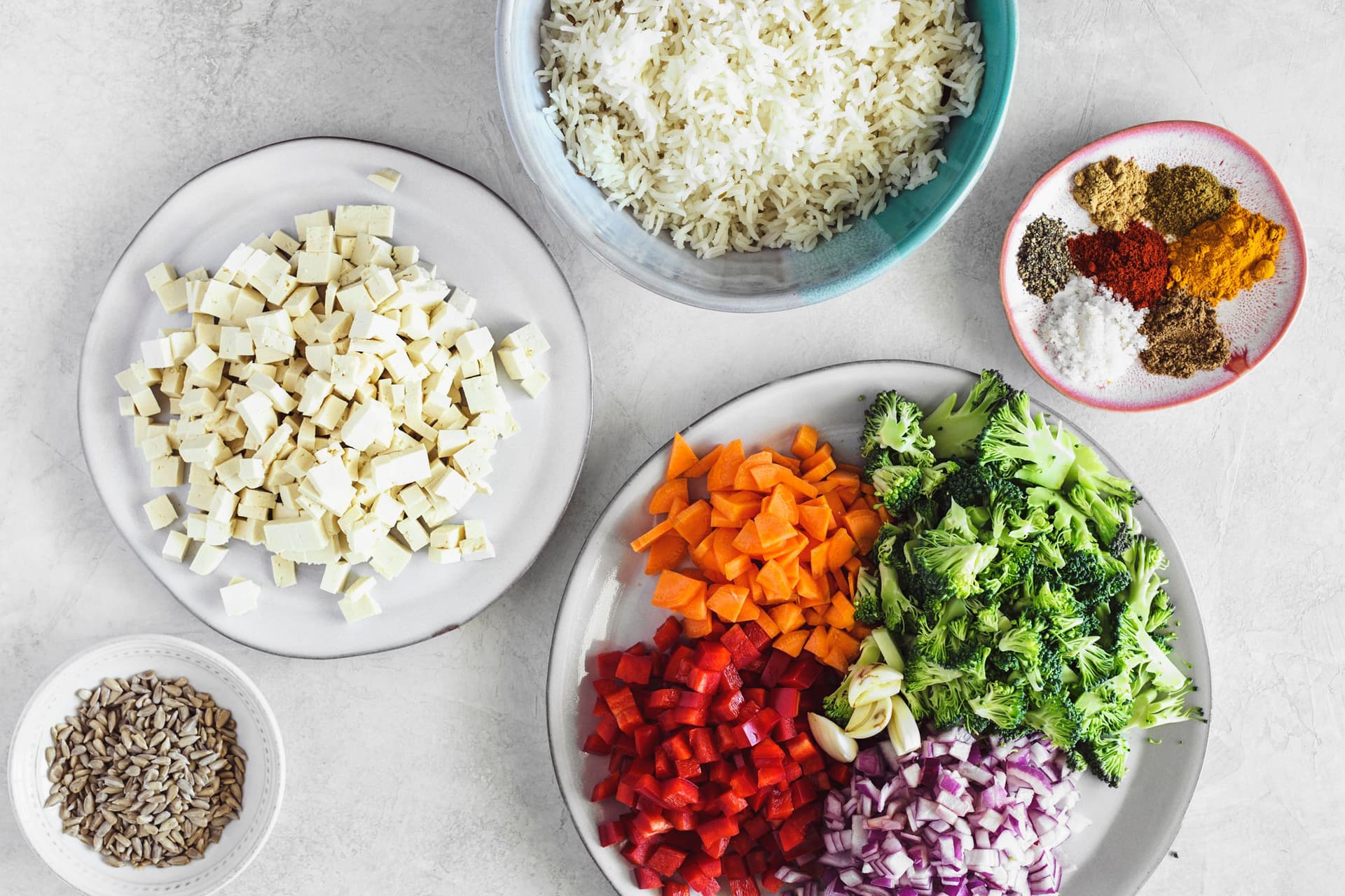 Taças com tofu em cubos, arroz, sementes de girassol, especiarias e vegetais picados prontos a cozinhar.