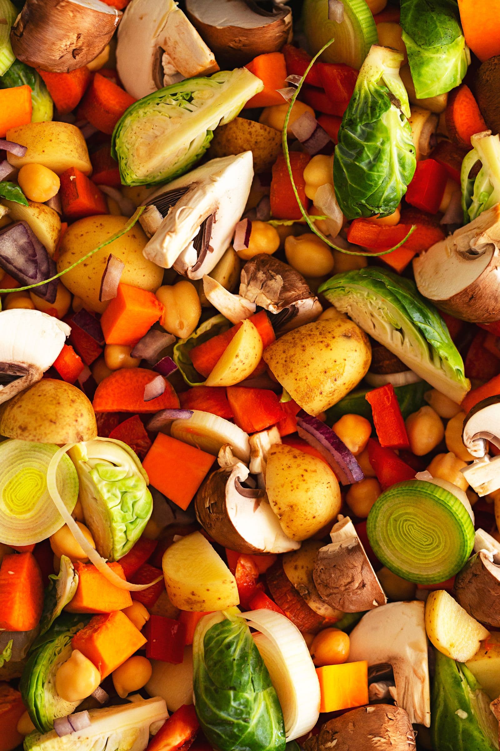 Raw mix of potatoes, carrots, Brussels sprouts, leeks, mushrooms and chickpeas ready to roast.