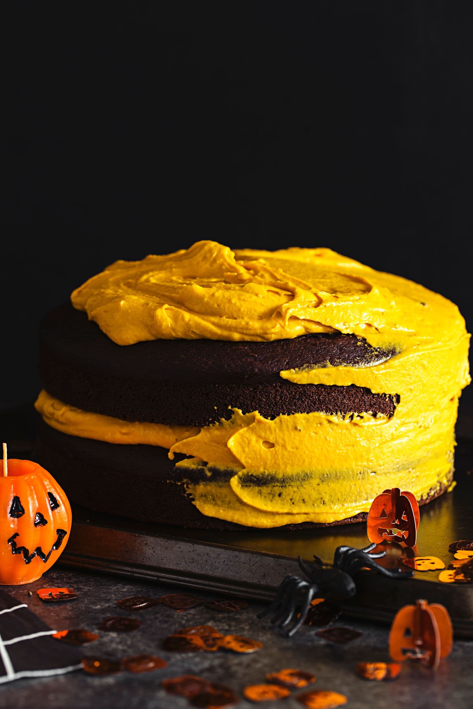 Layered chocolate and pumpkin cake topped with orange cashew “buttercream,” set against a Halloween-themed background.