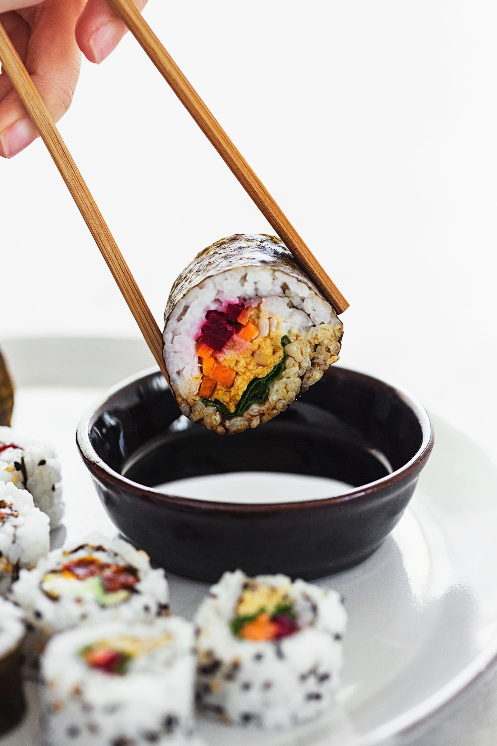 Vegan sushi roll being dipped into soy sauce with chopsticks.