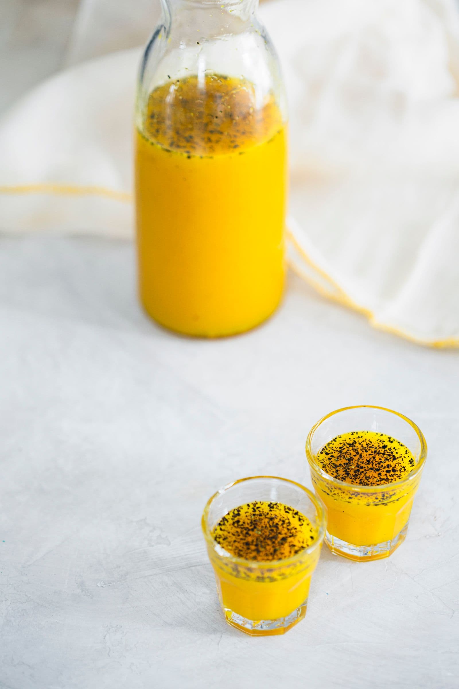 A glass bottle and two shot glasses filled with ginger turmeric syrup.