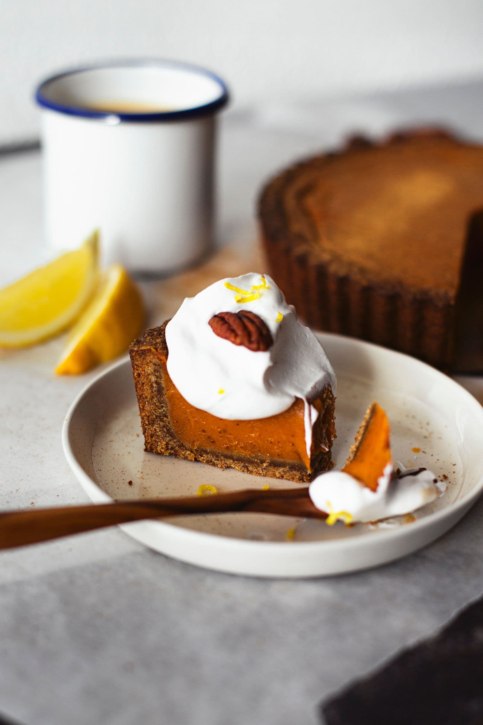 Prato com fatia de tarte de batata-doce e chantilly, com tarte inteira e gomo de limão ao fundo.
