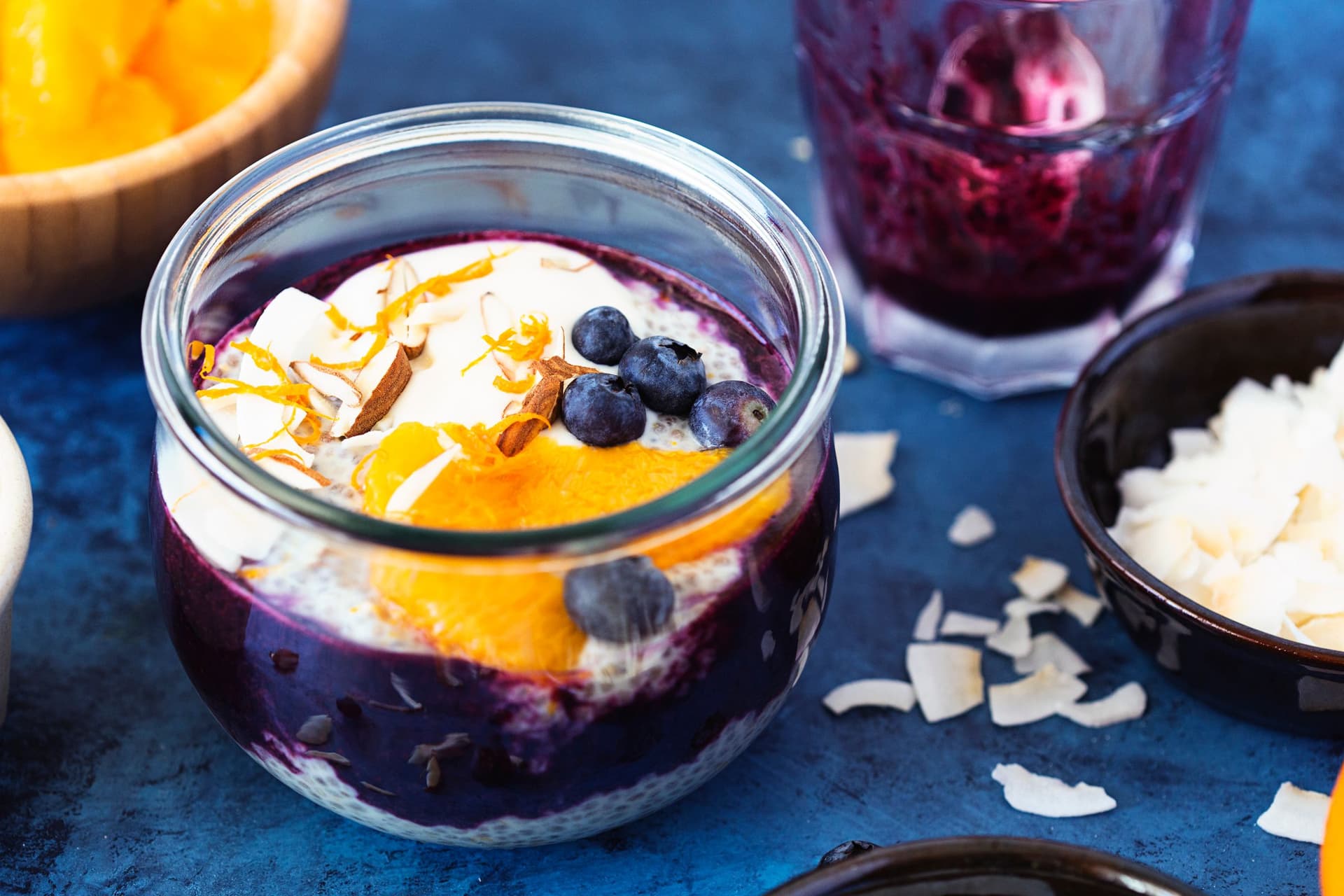 Frasco de pudim de chia com puré de mirtilo, fatias de laranja fresca e lascas de coco.
