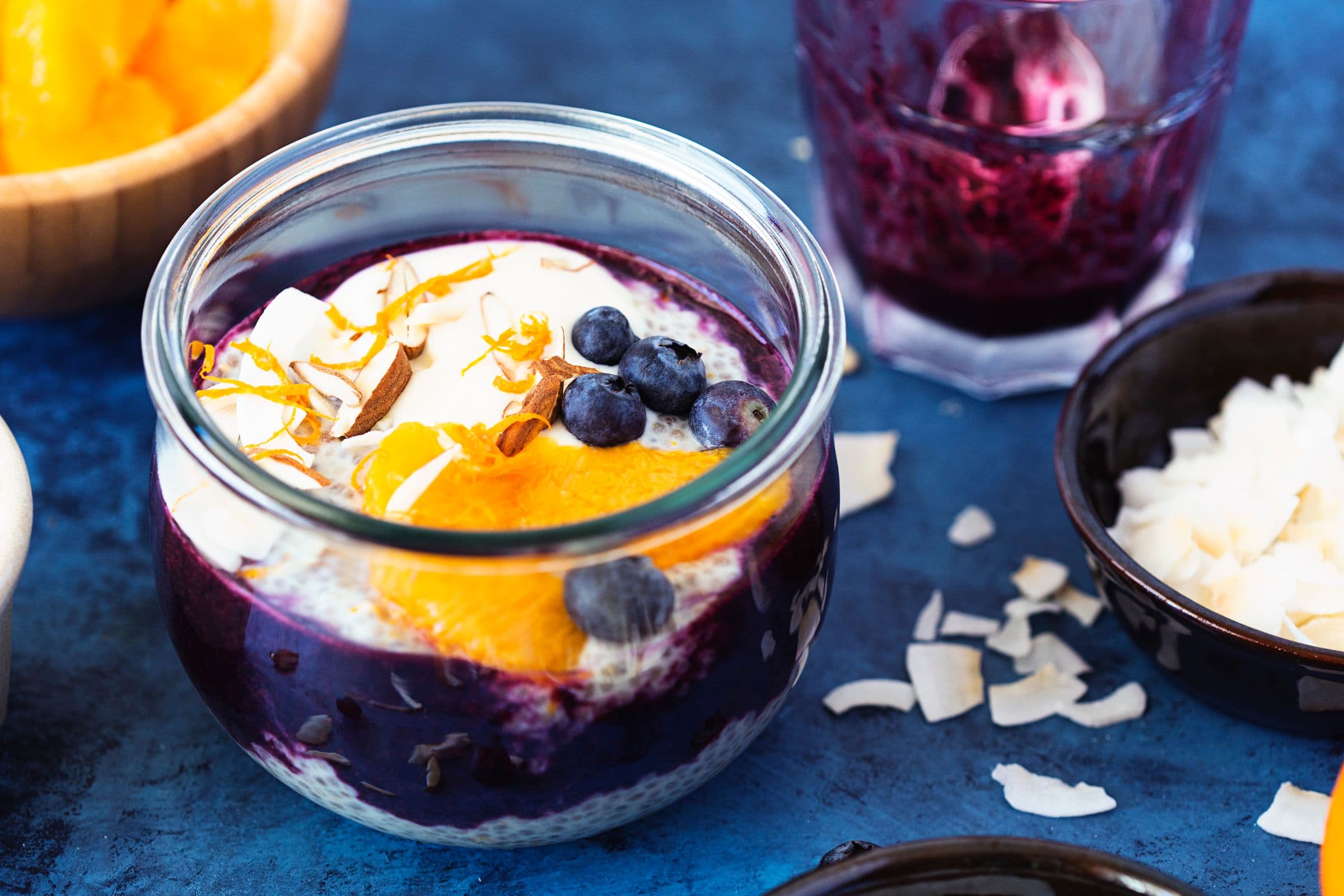 Frasco de pudim de chia com puré de mirtilo, fatias de laranja fresca e lascas de coco.