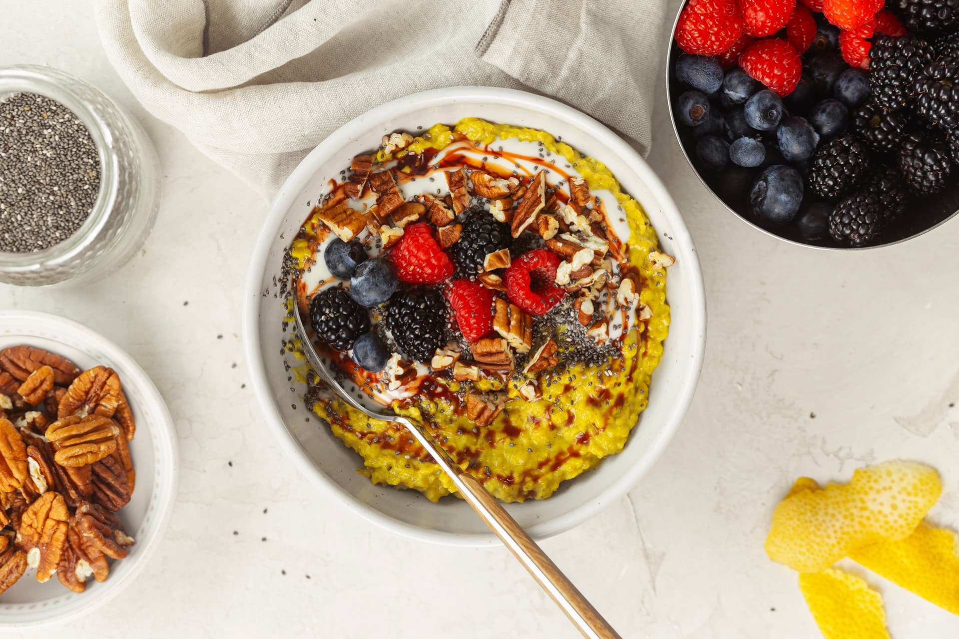 Papas douradas com chia, nozes pecan, frutos vermelhos, iogurte vegetal e xarope de tâmaras, numa taça branca com colher