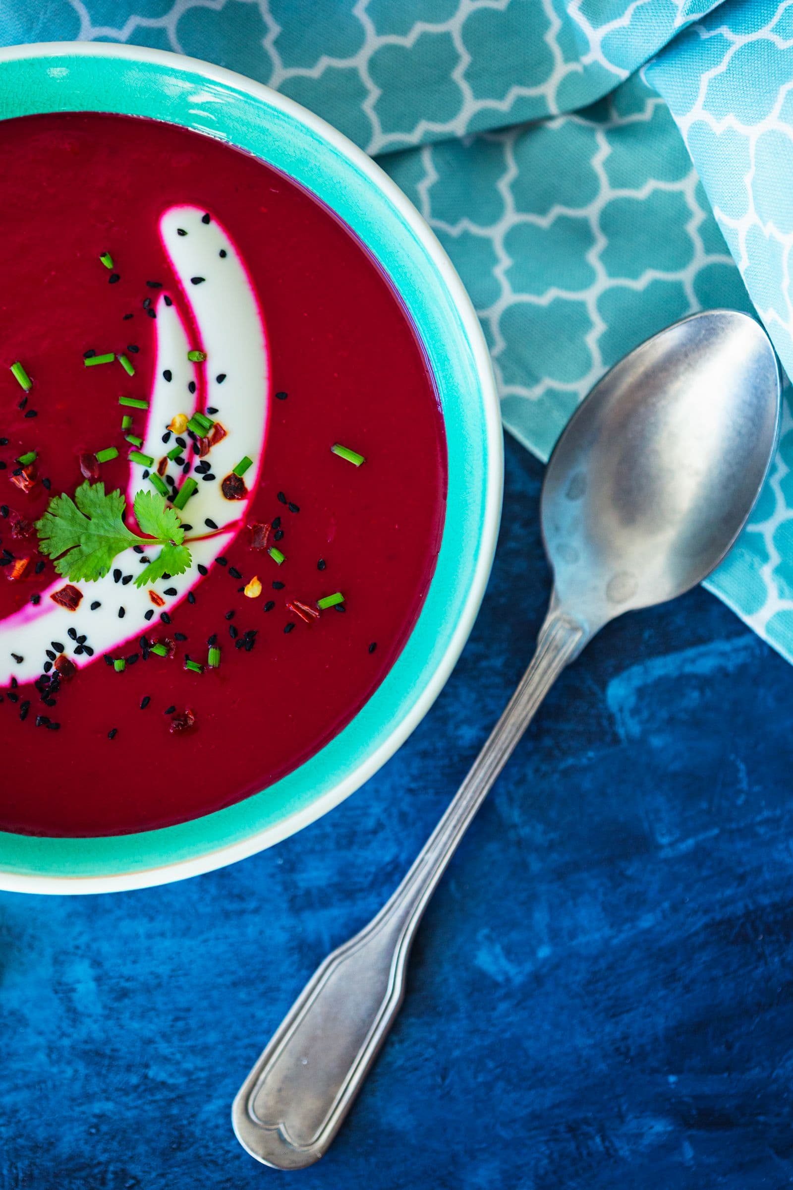 Close-up shot of bright beetroot soup garnished with cilantro and nigella seeds.