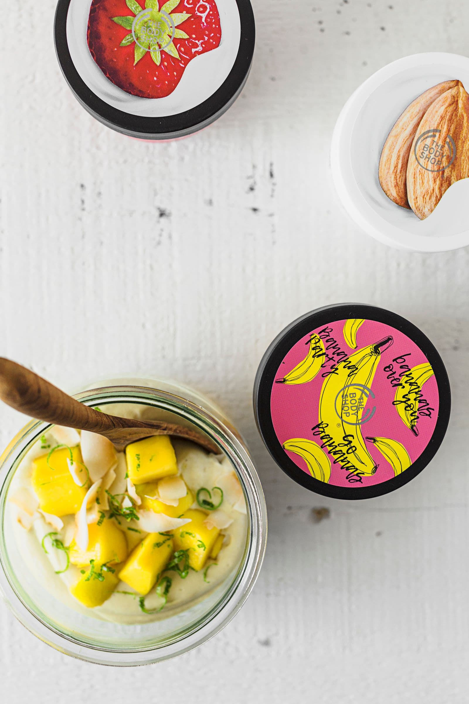 Jar of mango cashew yogurt beside The Body Shop Body Yogurt containers on a white table.