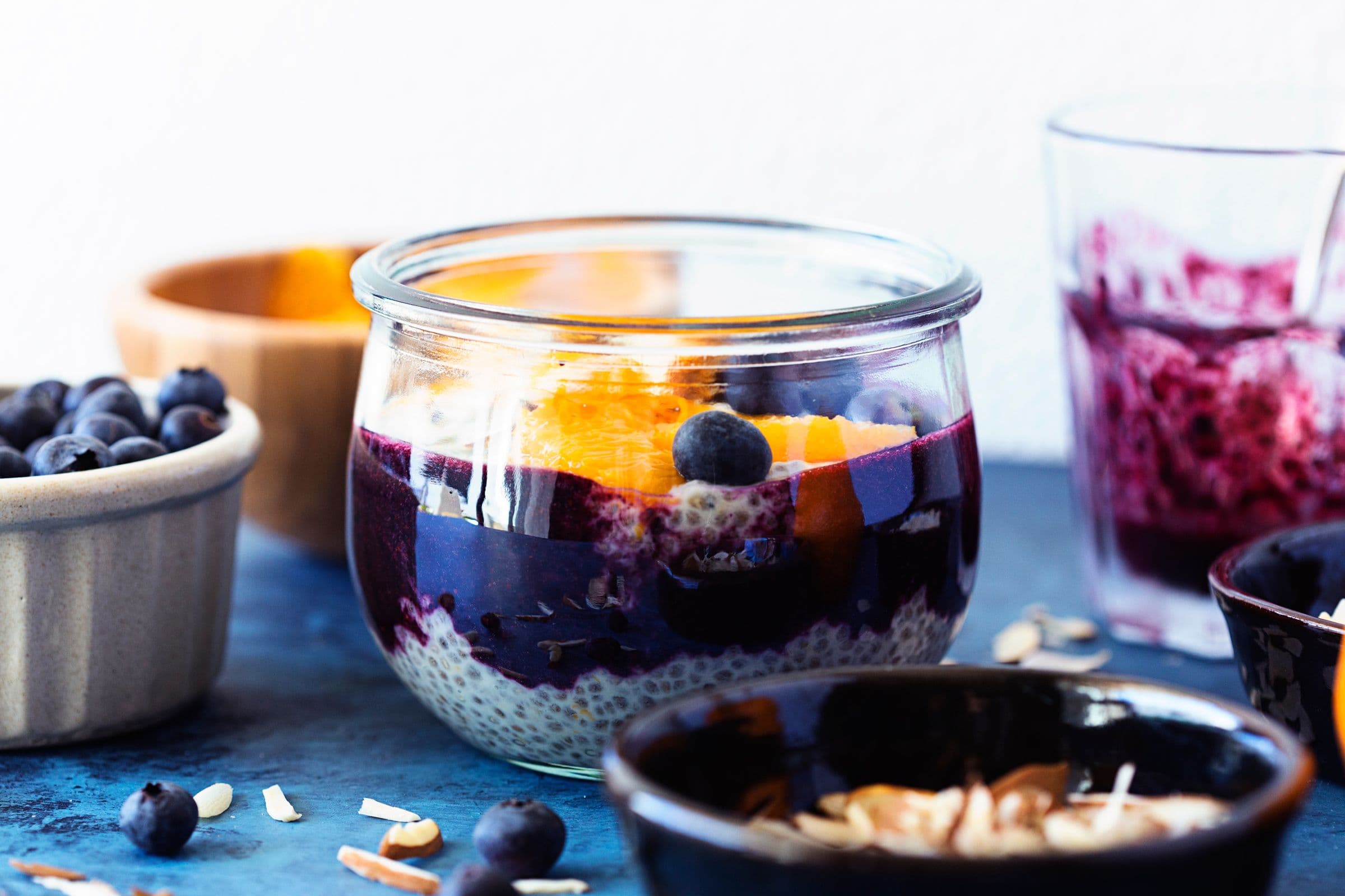 Frasco de vidro a mostrar as camadas de pudim de chia, puré de mirtilo e fatias de laranja.