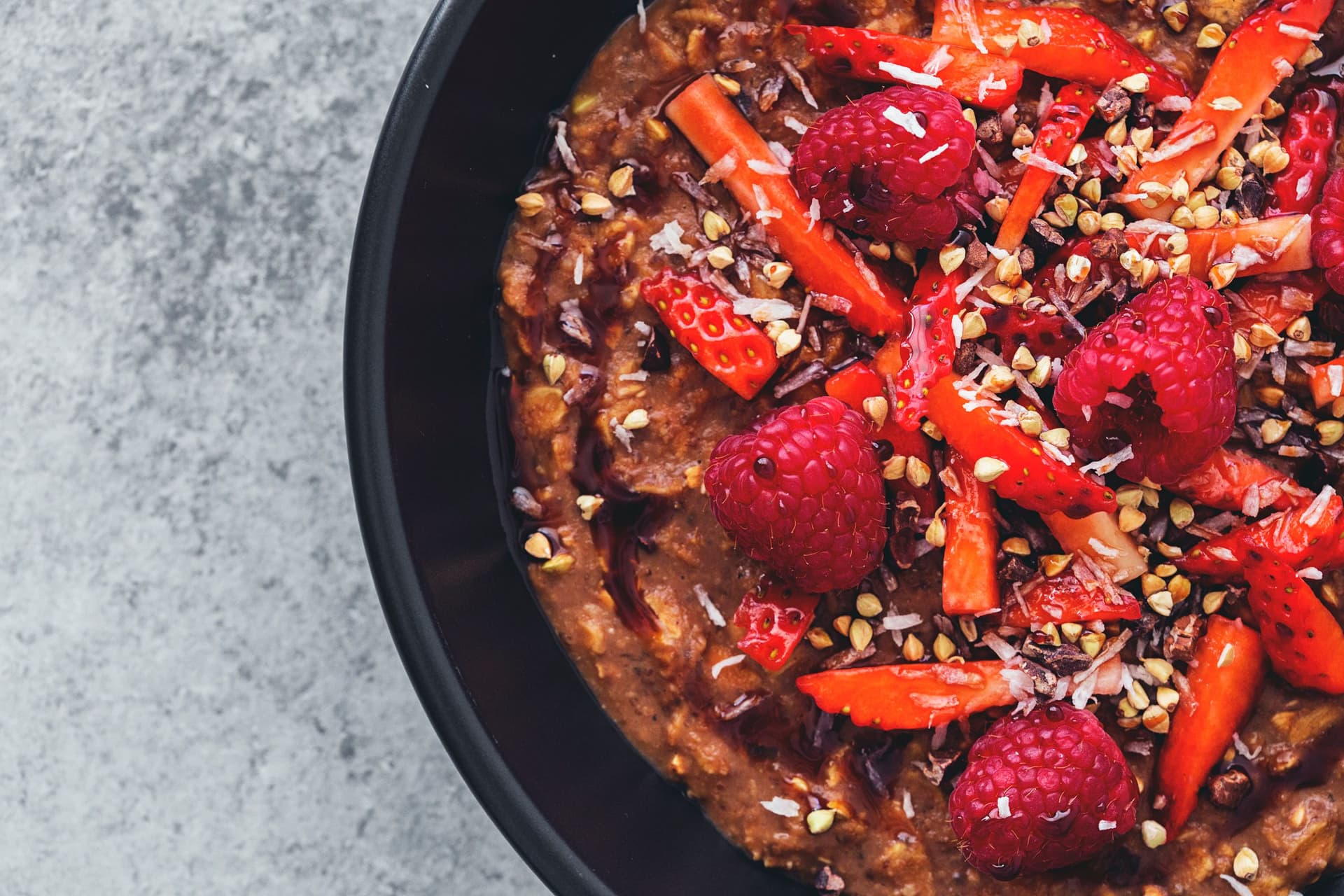 Detailed view of cacao oatmeal topped with raspberries, strawberries and crunchy buckwheat.