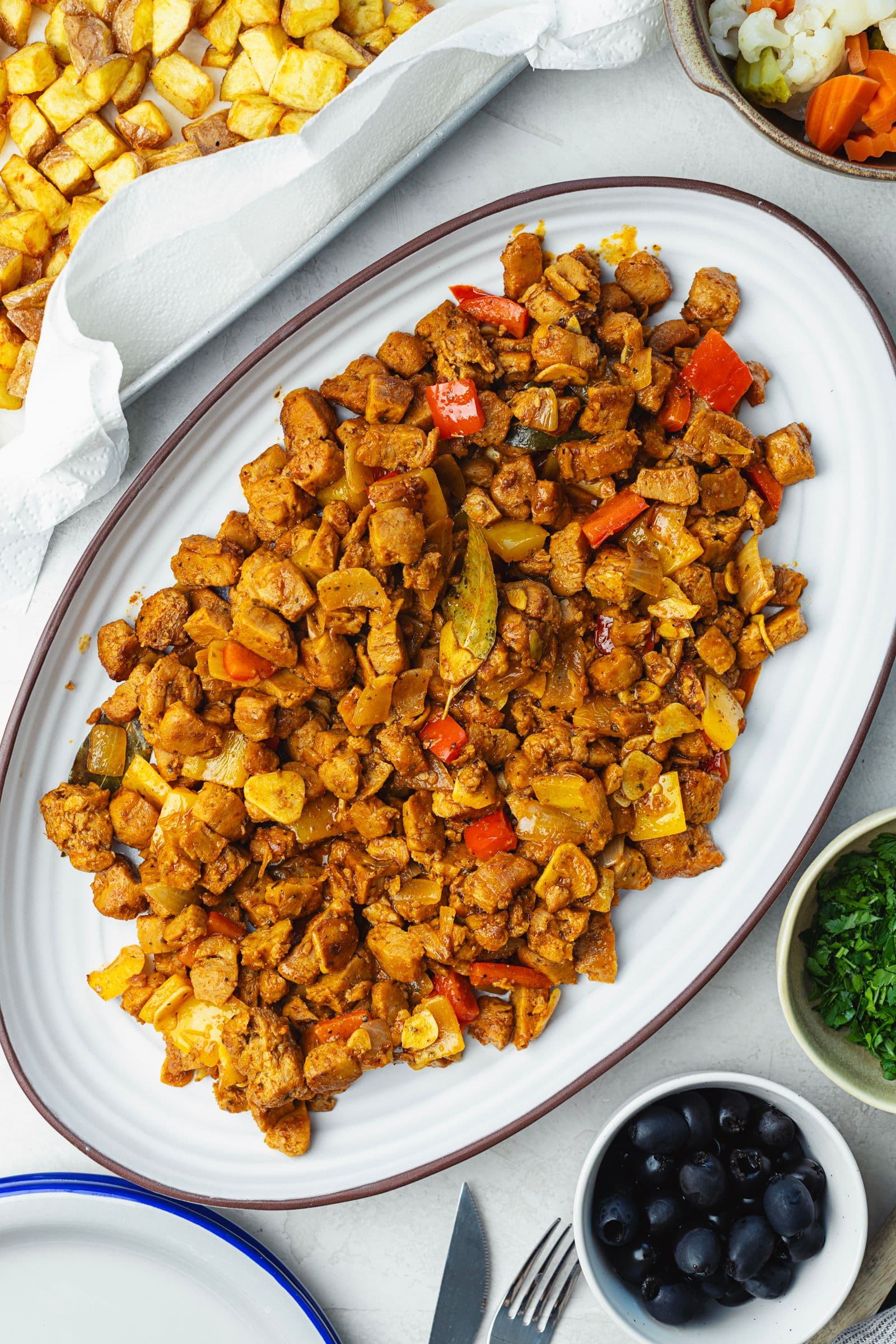 Travessa oval com pica pau de soja, soja caramelizada com pimentos e pickles, rodeada de batatas fritas, azeitonas e salsa picada ainda por juntar