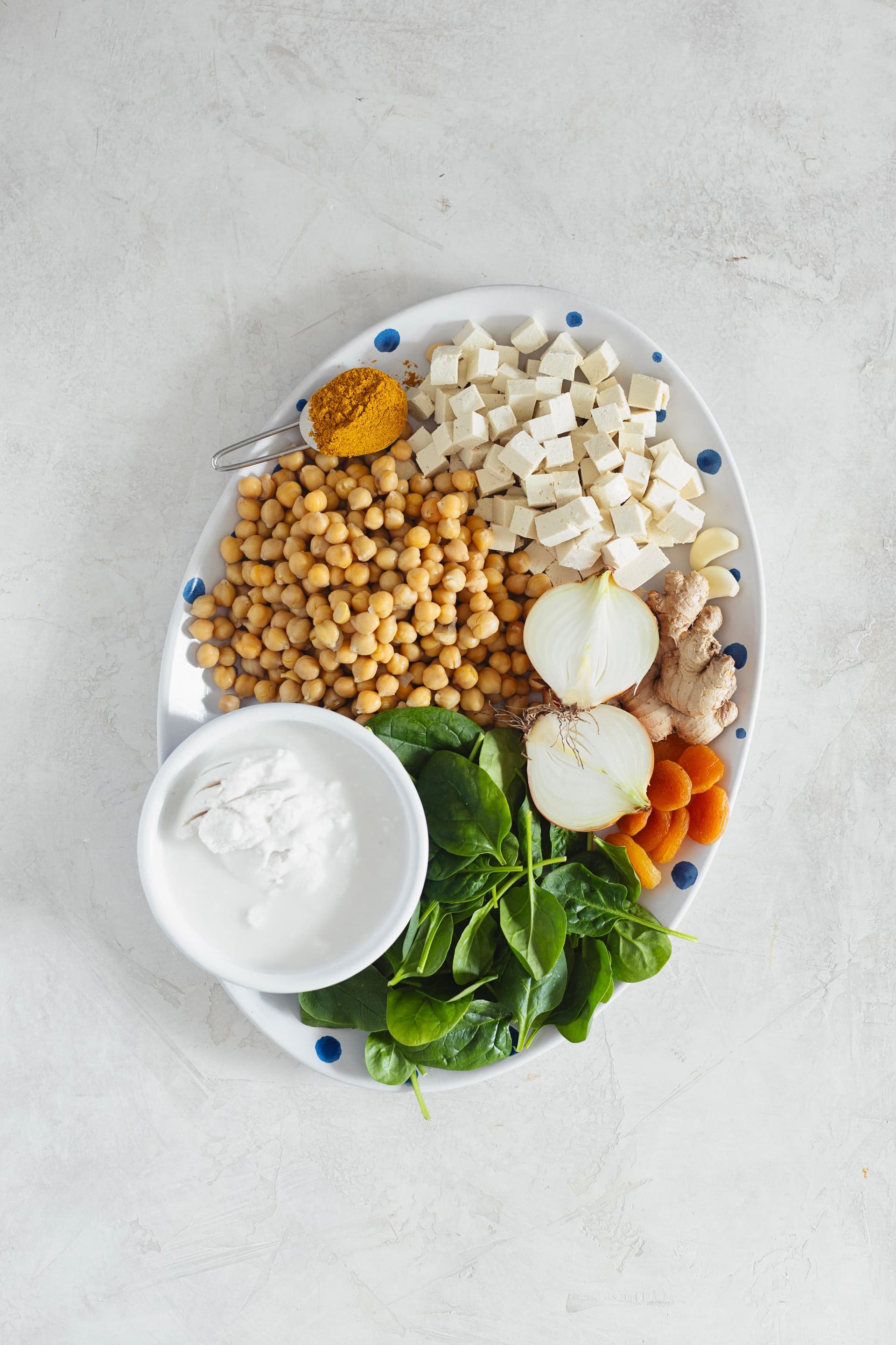 Overhead view of curry ingredients including chickpeas, tofu, onion, garlic, ginger, spinach, and coconut milk.