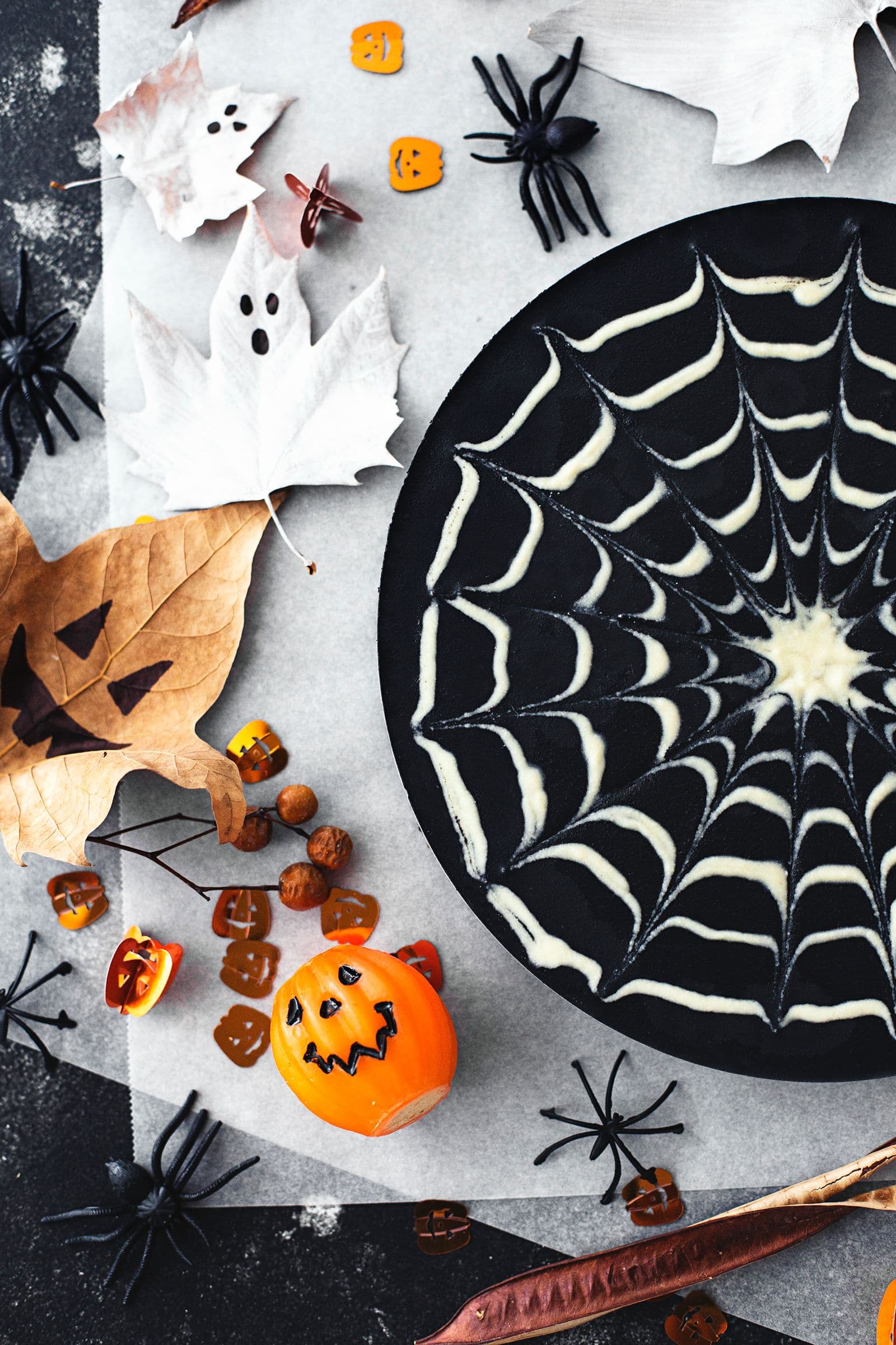 Mini pumpkins, spiders and autumn leaves painted as ghosts scattered around the Halloween dessert setup.