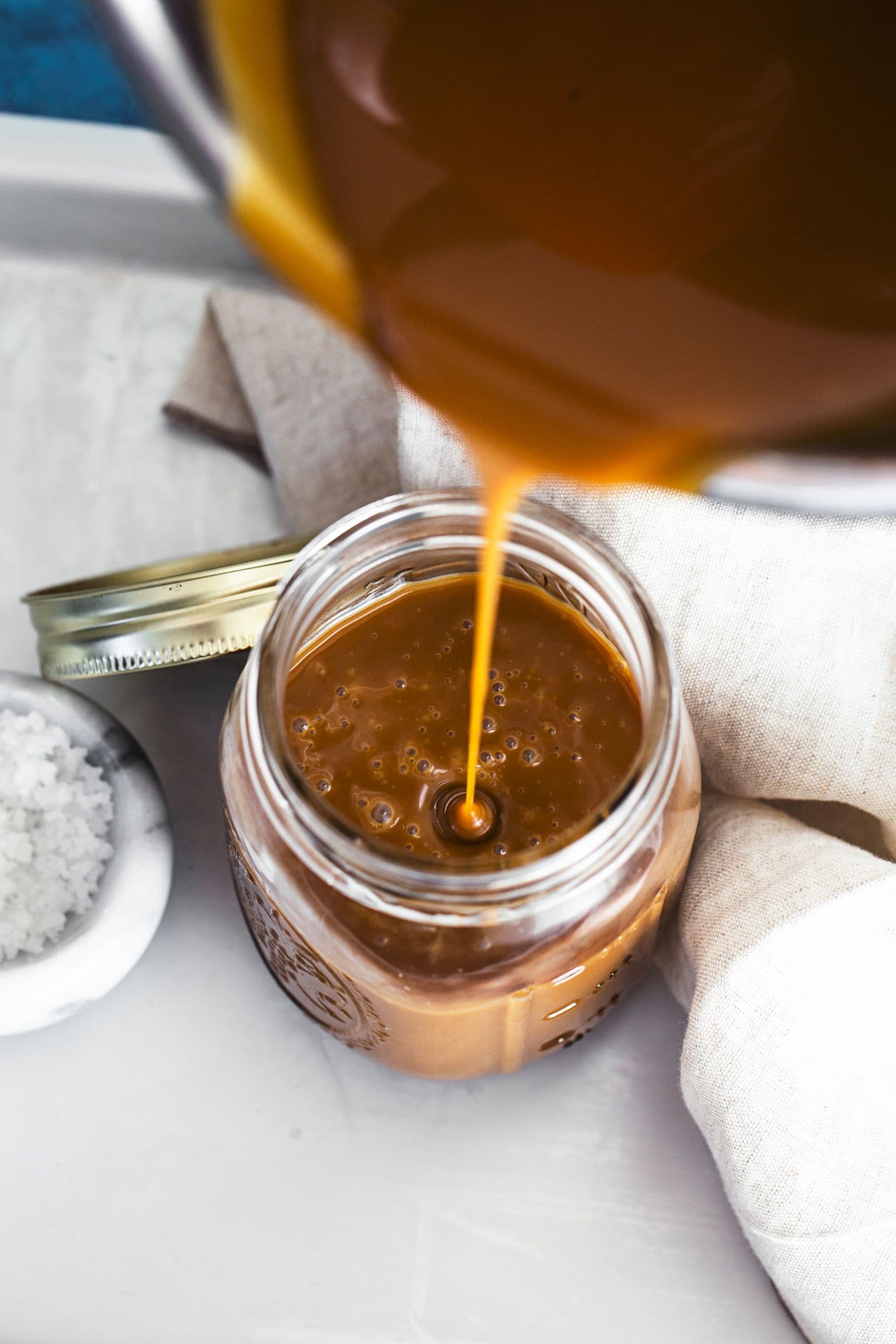 Vegan salted caramel being poured from a saucepan into a glass jar.