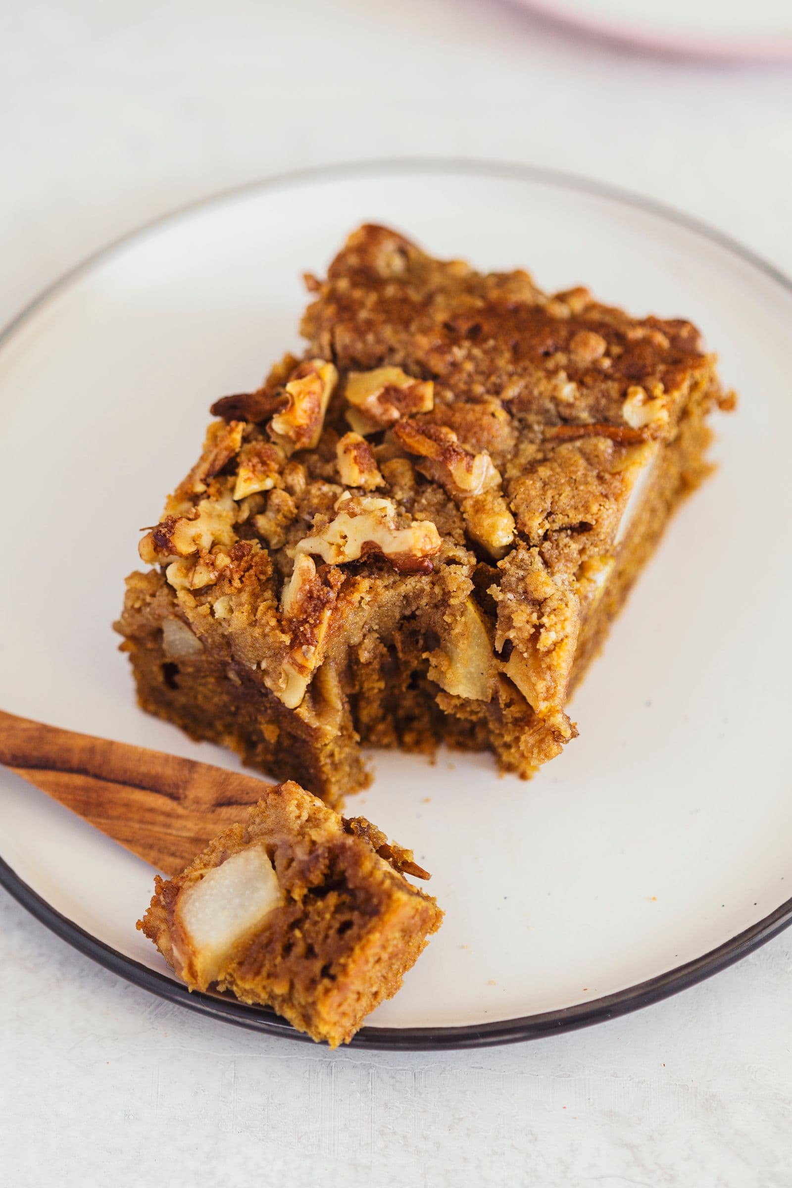 A slice of vegan coffee and pear coffee cake on a white plate with a wooden fork.