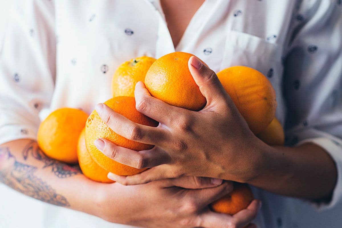 Person in a white shirt holding a large bundle of fresh oranges and lemons.