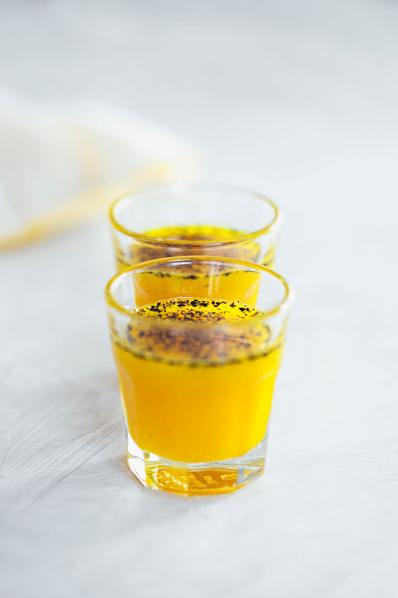 Copo com xarope de gengibre e curcuma de cor amarela vibrante, polvilhado com pimenta-preta moída.